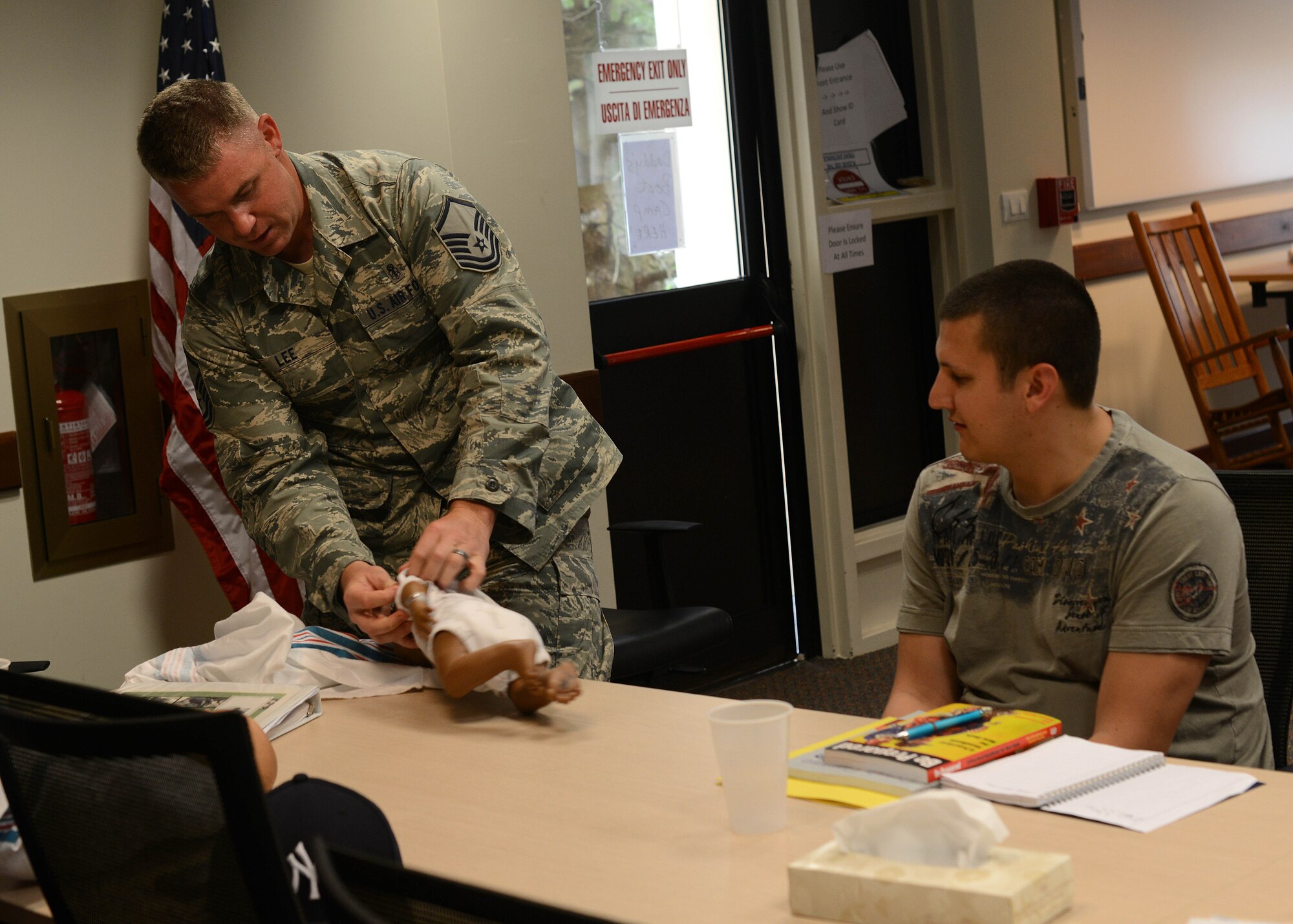 (From left) U.S. Air Force Master Sgt. Michael Lee, 31st Wing Staff Agencies self assesment program manager, speaks with Senior Airman Jeffrey McNamara, 31st Aircract Maintenance Squadron electronic warfare team lead, about how to remove a onesie during a Daddy Boot Camp course July 8, 2015, at Aviano Air Base, Italy.  The program aims to teach fathers about infant care including calming and soothing, how to respond to possible changes and concerns. (U.S. Air Force photo by Staff Sgt. Evelyn Chavez)