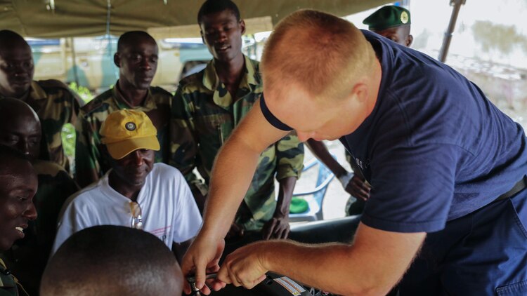 U.S. Coastguard Machinery Technician 1st Class Shawn Dillman, a small boat maintenance instructor assigned to Special-Purpose Marine Air-Ground Task Force Crisis Response-Africa, demonstrates proper boat engine maintenance techniques to a group of Compagnie Fusilier de Marin Commandos in St. Louis, Senegal, June 30, 2015. Approximately 20 U.S. Marines, sailors and coast guardsmen with the unit spent the week teaching and training more than 30 members of the Fusilier Marins small-boat operations and maintenance skills. 