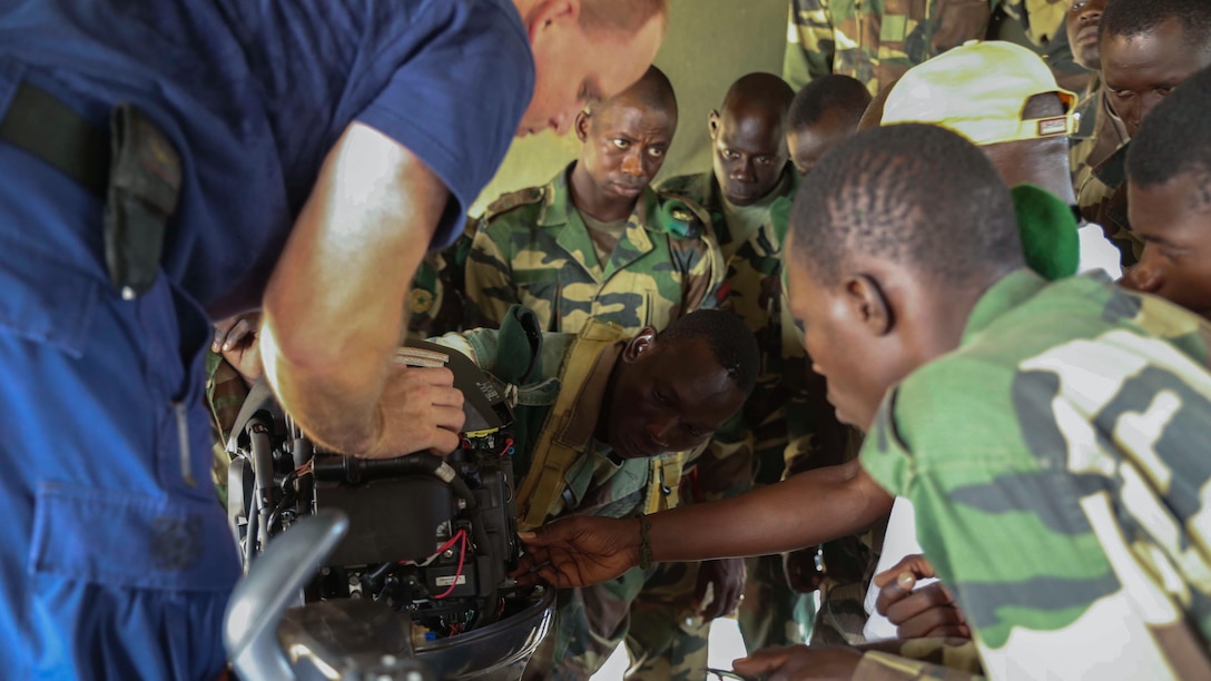 U.S. Coastguard Machinery Technician 1st Class Shawn Dillman, a small boat maintenance instructor assigned to Special-Purpose Marine Air-Ground Task Force Crisis Response-Africa, demonstrates proper boat engine maintenance techniques to a group of Compagnie Fusilier de Marin Commandos in St. Louis, Senegal, June 30, 2015. Approximately 20 U.S. Marines, sailors and coast guardsmen with the unit spent the week teaching and training more than 30 members of the Fusilier Marins small-boat operations and maintenance skills. 