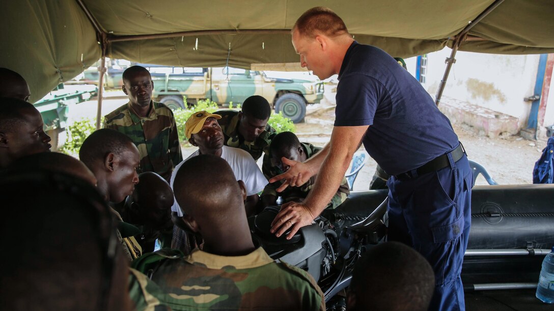U.S. Coastguard Machinery Technician 1st Class Shawn Dillman, a small boat maintenance instructor with Special-Purpose Marine Air-Ground Task Force Crisis Response-Africa, teaches a group of Compagnie Fusilier de Marin Commandos basic boat engine maintenance procedures in St. Louis, Senegal, June 30, 2015. Approximately 20 U.S. Marines, sailors and coast guardsmen with the unit spent the week teaching and training more than 30 members of the Fusilier Marins small-boat operations and maintenance skills.