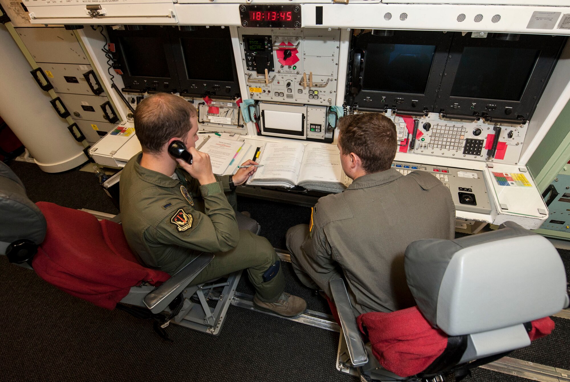 1st Lt. Trey Morris, 740th Missile Squadron combat crew commander, answers the phone as 1st Lt. Daniel Morris, 740th MS deputy combat crew commander reviews a binder at the Bravo 01 Missile Alert Facility, July 1, 2015. The 740th MS maintains the missile force around-the-clock and controls 50 launch facilities and five missile alert facilities within their area of the missile complex. (U.S. Air Force photo/Senior Airman Stephanie Morris)