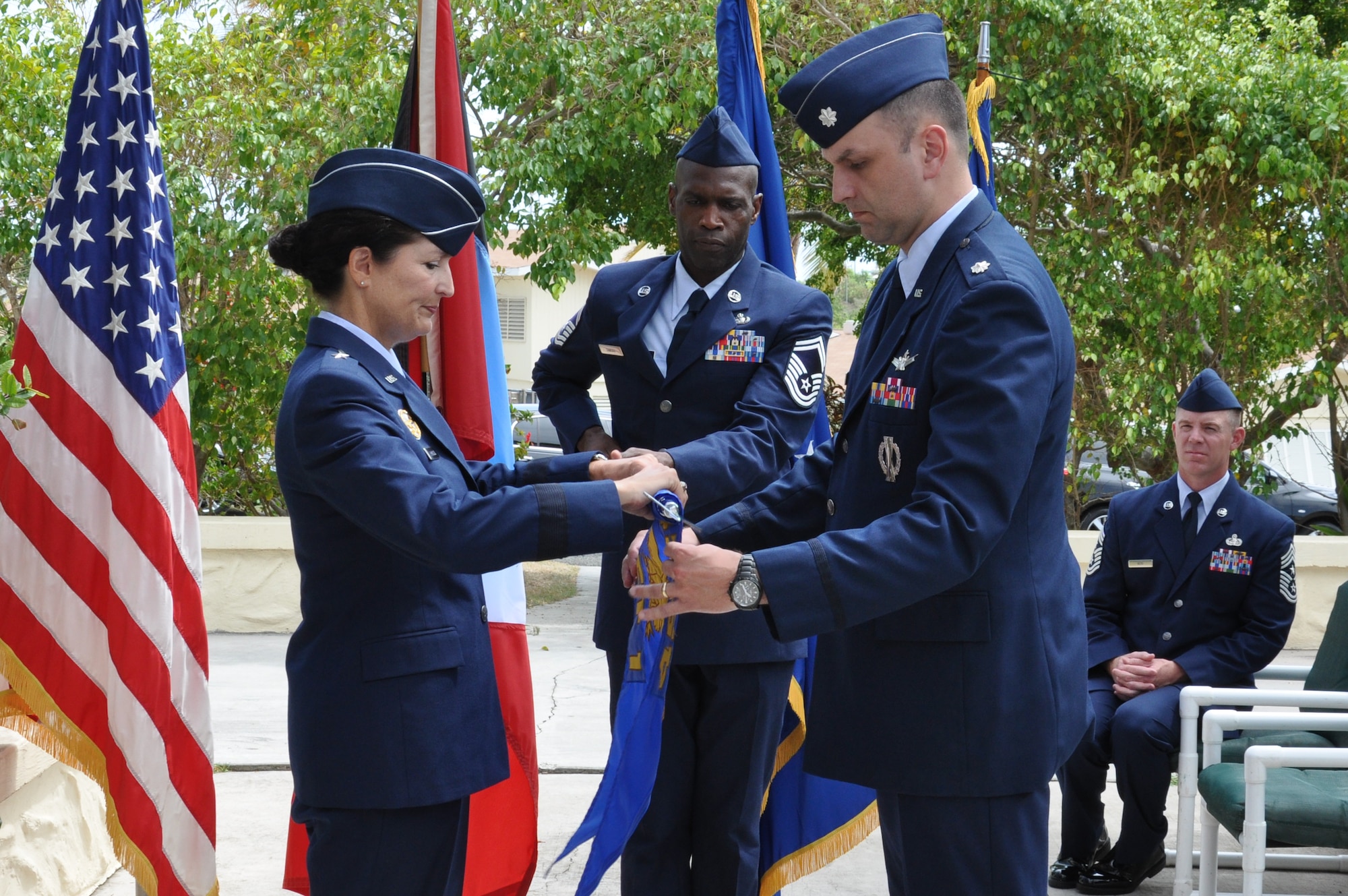 Brig. Gen. Nina Armagno, 45th Space Wing commander and presiding officer, ceremoniously rolls up the Detachment 1 guidon with assistance from Lt. Col. Steven Melvin, Det 1, 45th Operations Group commander, while Senior Master Sgt. Kwame Tawiah, Det 1, 45th OG superintendent, center, holds the guidon steady and Chief Master Sgt. Craig Neri, 45th SW command chief, back, observes during the deactivation ceremony of Antigua Air Station July 7, 2015, in Antigua. Rolling and sheathing the detachment colors in a sleeve symbolizes the organizations inactive status. (U.S. Air Force photo by 1st Lt. Alicia Wallace)(Released)