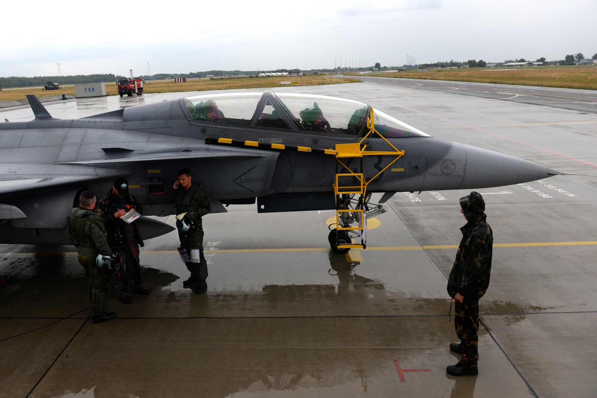 Hungarian and Swedish air force JAS-39 Gripen pilots and aircraft maintainers shield themselves from rain while performing a pre-flight inspection June 24, 2015, during air refueling familiarization training on Kecskemét air base, Hungary. Hungarian, U.S. and Swedish air force personnel met for a two-week familiarization period enabling the Hungarian JAS-39 Gripen pilots to successfully perform air refueling for the first time. (U.S. Air Force photo by Senior Airman Kate Thornton/Released)
