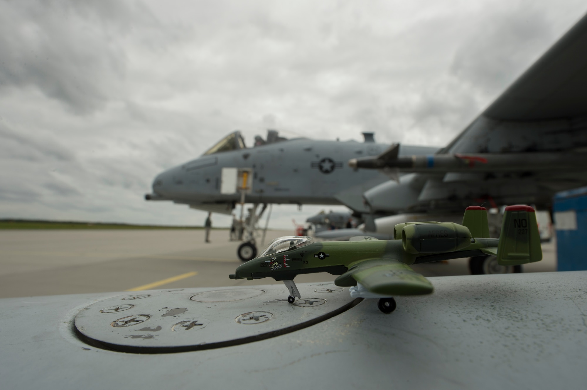 A forest camouflaged A-10 Thunderbolt II attack aircraft replica rests on a fuel tank near a U.S. Air Force A-10 Thunderbolt II attack aircraft assigned to the 354th Expeditionary Fighter Squadron during a theater security package deployment at Lask Air Base, Poland, July 10, 2015. The U.S. Air Force’s forward presence in Europe allows cooperation among NATO allies and partners to develop and improve ready air forces capable of maintaining regional security. (U.S. Air Force photo by Staff Sgt. Christopher Ruano/Released)