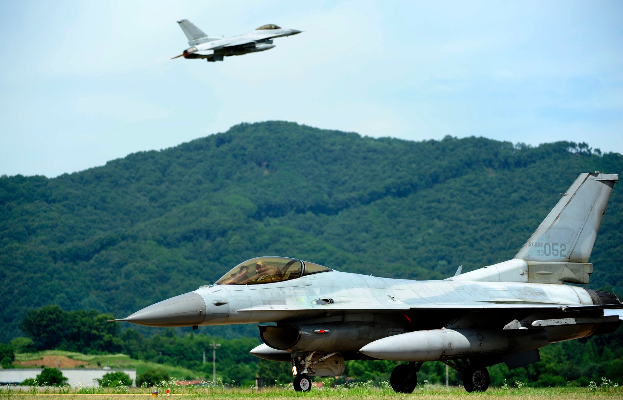 A KF-16 Fighting Falcon from the 19th Fighter Wing taxis as another takes off of the runway at Jungwon Air Base, Republic of Korea, during Buddy Wing 15-6, July 8, 2015. In an effort to enhance U.S. and ROKAF air combat capability, Buddy Wing exercises are conducted multiple times throughout the year on the peninsula to sharpen interoperability between the allied forces so that if need be, they are always ready to fight as a combined force. (U.S. Air Force photo by Staff Sgt. Nick Wilson/Released)