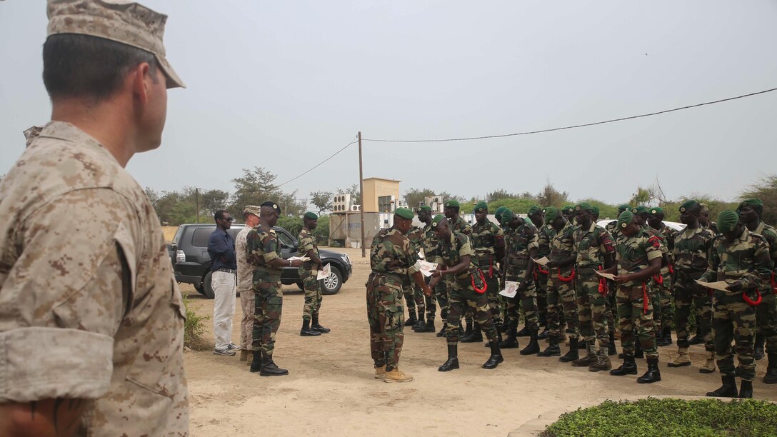 U.S. Marine Staff Sgt. Anthony Rowan, the staff-noncommissioned officer in charge of a theater security cooperation team from Special-Purpose Marine Air-Ground Task Force Crisis Response-Africa, looks on as Compagnie Fusilier de Marin Commandos receive certificates during a graduation ceremony in St. Louis, Senegal, July 9, 2015. More than 30 members of the Fusilier Marins graduated a nearly six-week long maritime security force assistance training course. 