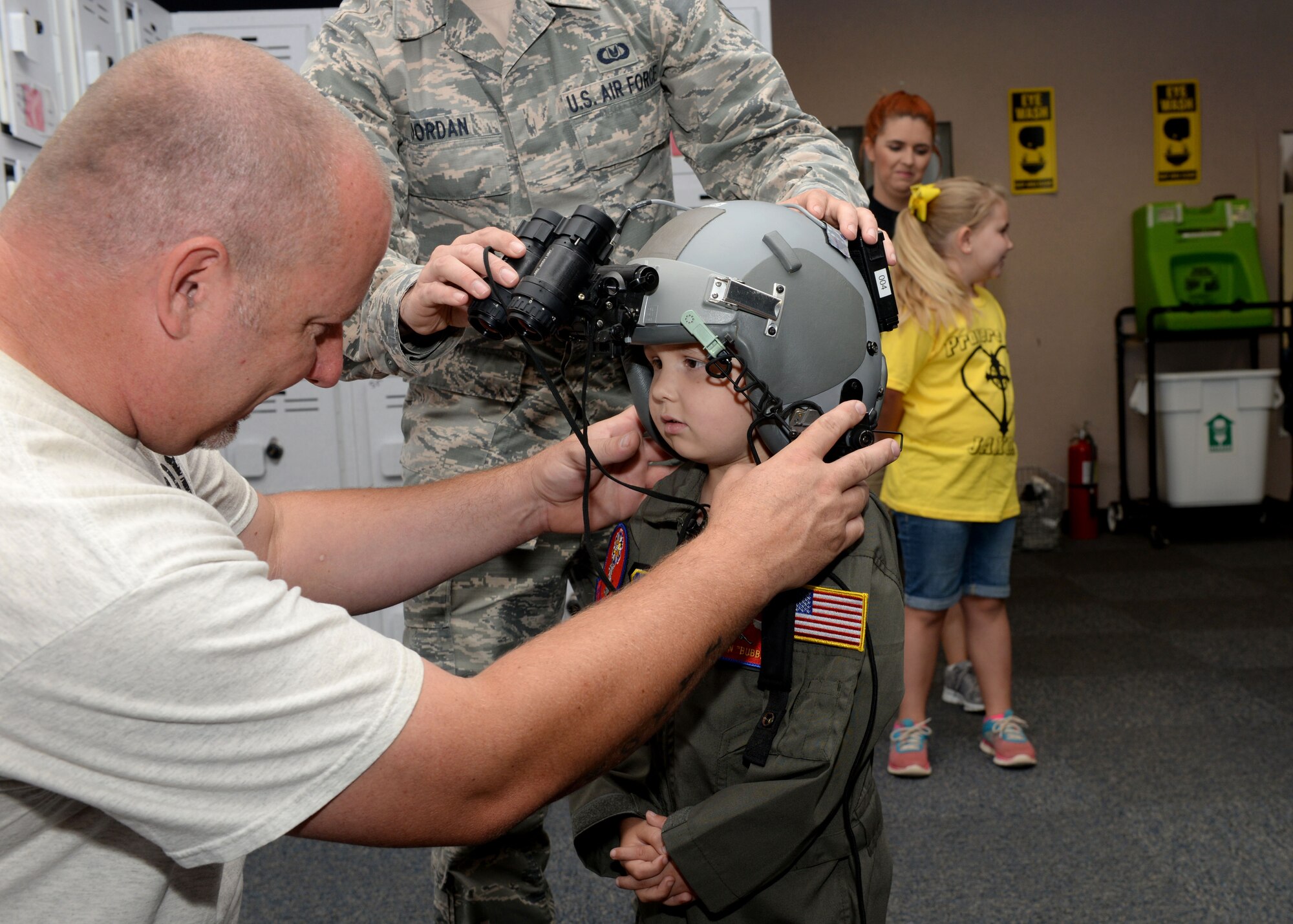 ALTUS AIR FORCE BASE, Okla. – Cody Dugger helps his son, Jaxon, put on a flight helmet equipped with nightvision goggles at the 97th Operations Support Squadron, June 26, 2015. Jaxon was diagnosed with Ewing’s sarcoma when he was two years old. (U.S. Air Force photo by Airman 1st Class Kirby Turbak/Released)