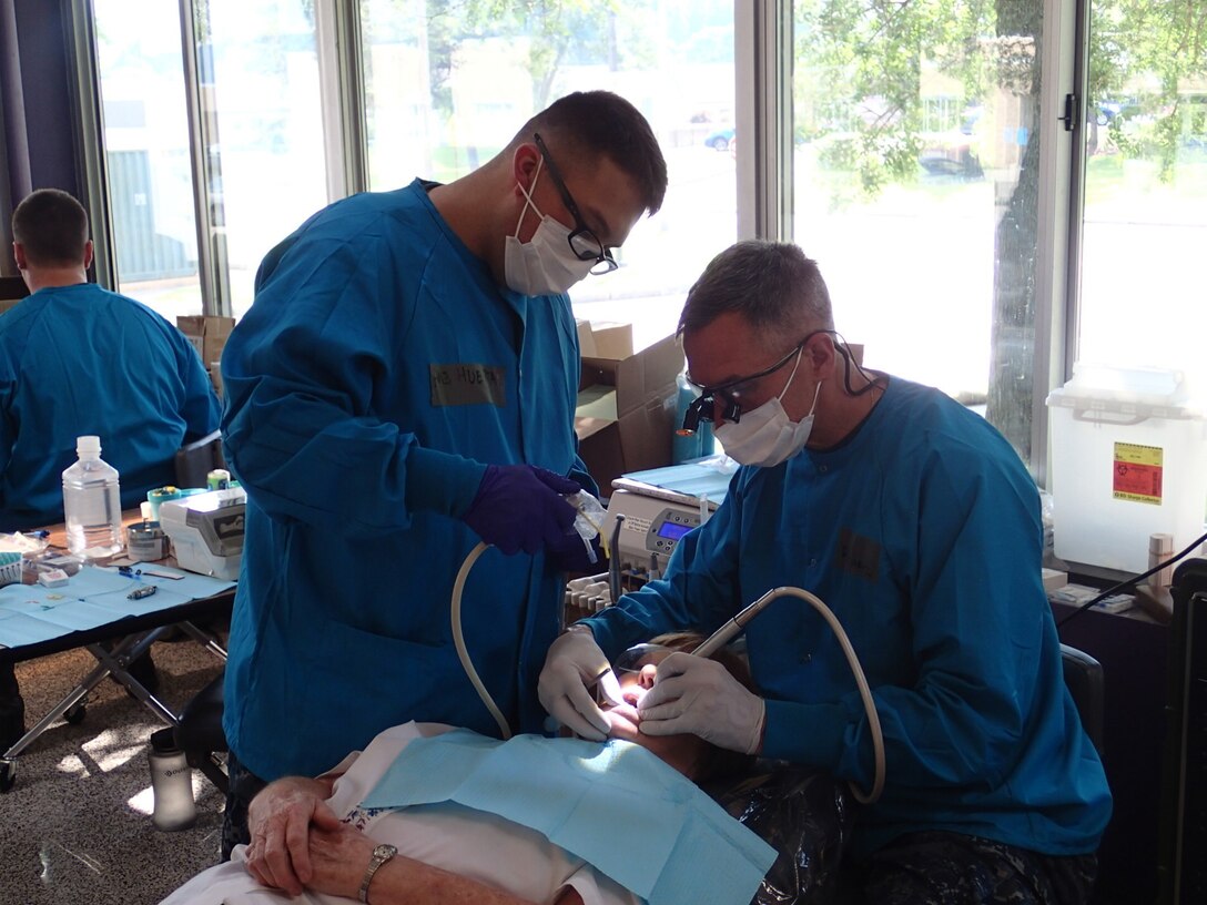 Lt. Cmdr. Walter Schratz, right, a dentist and Petty Officer 3rd Class Erick Huertas, a dental tech, both from EMF Bethesda provide dental care at Greater Chenango Cares, July 12, 2015. Greater Chenango Cares is one of the Innovative Readiness Training missions which provides real-world training in a joint civil-military environment while delivering world class medical care to the people of Chenango County, N.Y., from July 13-23. (U.S. Army photo by Sgt. Jennifer Shick/released)