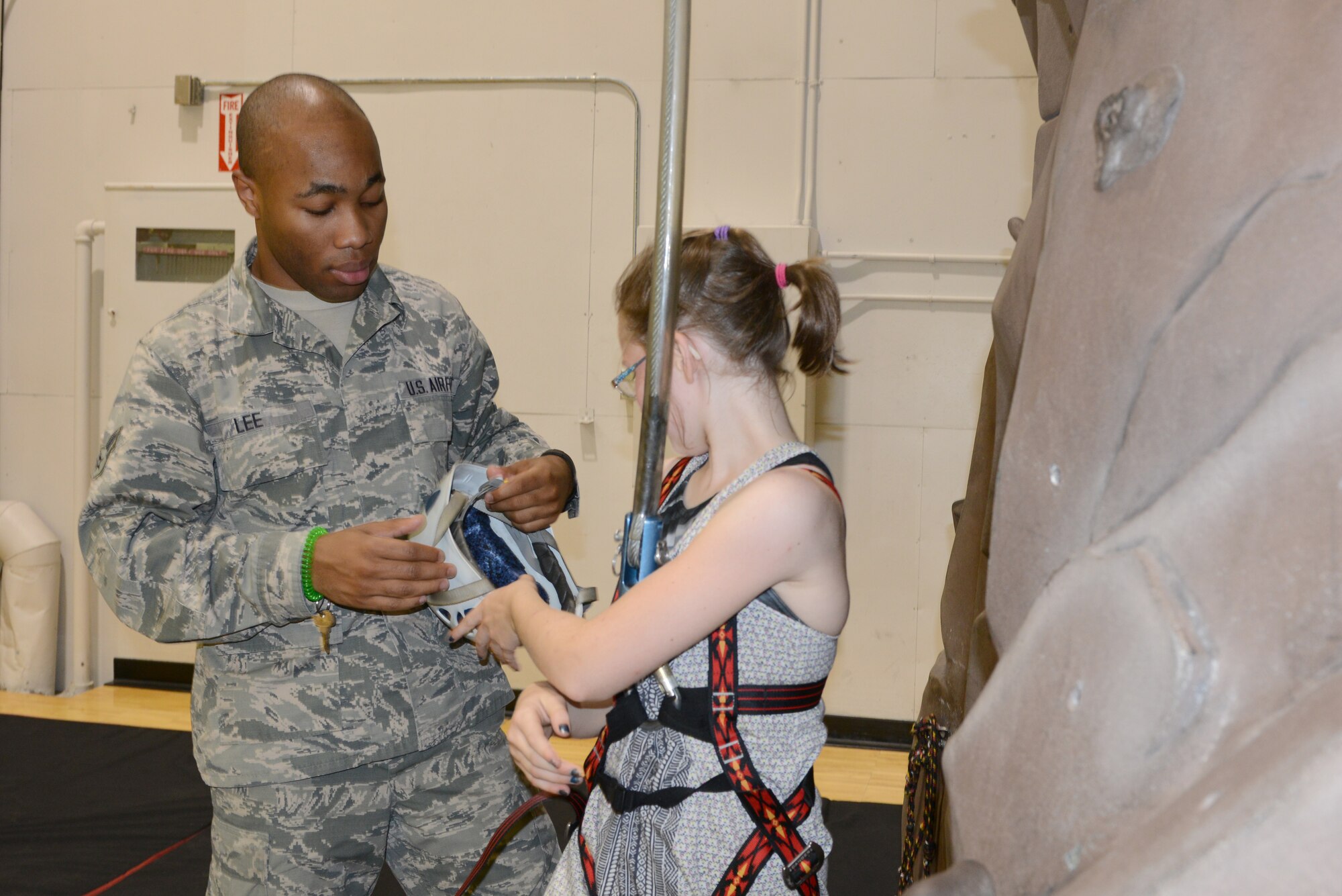 U.S. Air Force Airman 1st Class Lazrus Lee, a 354th Force Support Squadron fitness specialist, assists Katie Hauer as she puts on rock climbing gear, July 13, 2015, in the Baker Field House, at Eielson Air Force Base, Alaska. As a fitness specialist, Lee helps to maintain a safe environment for people when they exercise. (U.S. Air Force photo by Senior Airman Ashley Nicole Taylor/Released)