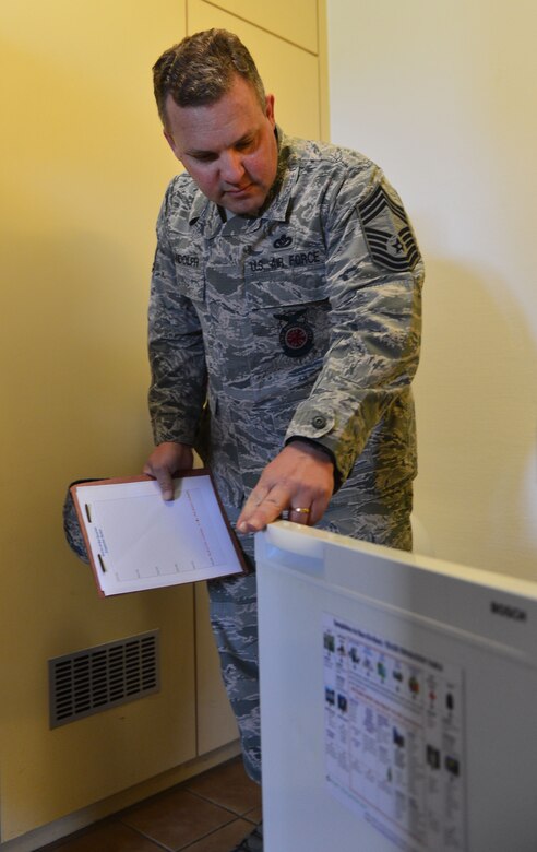 U.S. Air Force Chief Master Sgt. Timothy Randolph, installation fire chief, inspects the inside of a refrigerator as part of a walkthrough of Dorm 225 during the Dorm of the Quarter competition at Spangdahlem Air Base, Germany, July 8, 2015. The first round of the competition was graded by a panel of four judges, with the top three dorms making it through to the final round later in the day. (U.S. Air Force photo by 2nd Lt Meredith Mulvihill/Released)