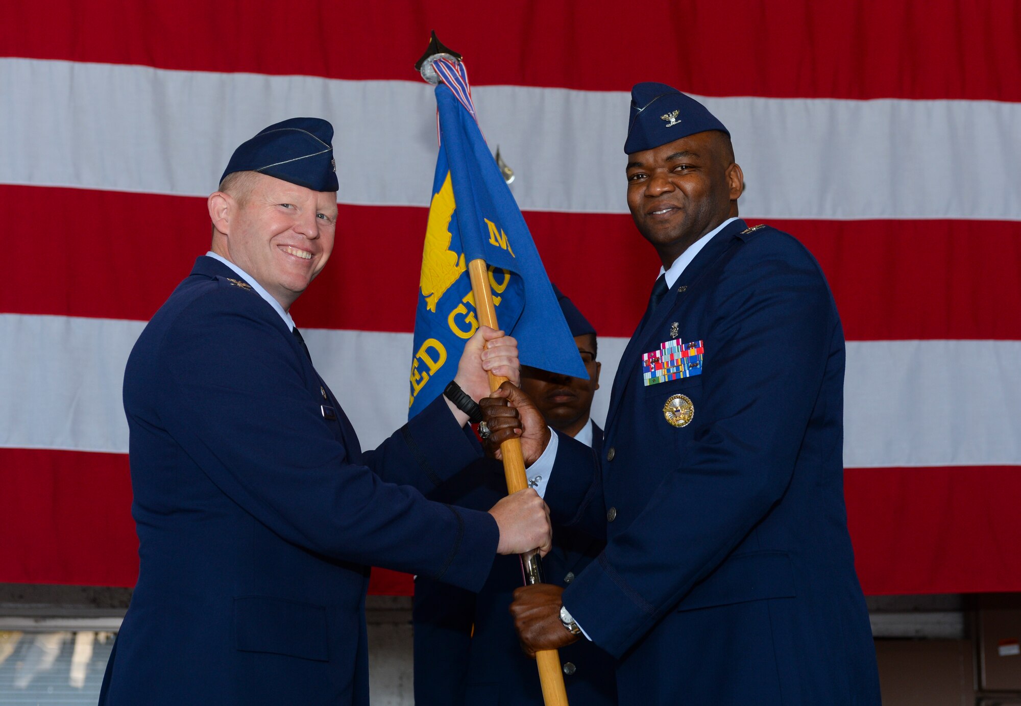 U.S. Air Force Col. Joe McFall, 52nd Fighter Wing commander, hands the 52nd Medical Group's ceremonial guidon to U.S. Air Force Col. Alfred Flowers, incoming 52nd MDG commander, during the 52nd MDG's change of command ceremony at Hangar One on Spangdahlem Air Base, Germany, July 10, 2015. Flowers assumed command from outgoing commander U.S. Air Force Col. Jill Scheckel. (U.S. Air Force photo by Staff Sgt. Joe W. McFadden/Released)