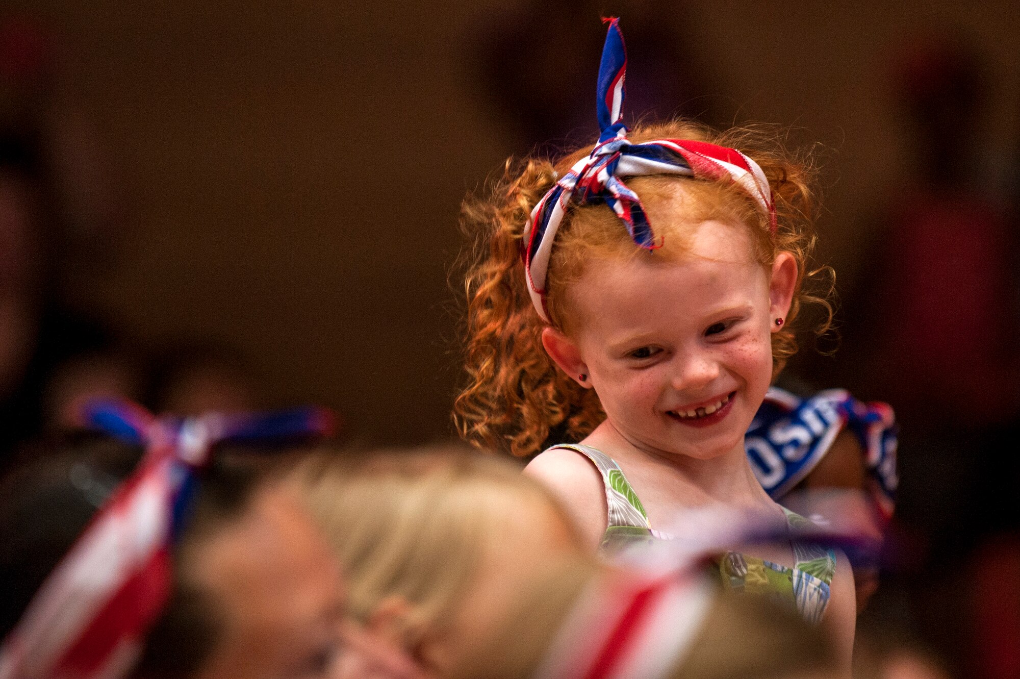 A military child smiles during a performance for the 2015 Sesame Street/USO Experience for Military Families tour, inside the Skelton Memorial Fitness Center July 11, 2015, at Spangdahlem Air Base, Germany. The tour based their shows on the experiences of military children. (U.S. Air Force photo by Senior Airman Rusty Frank/Released)