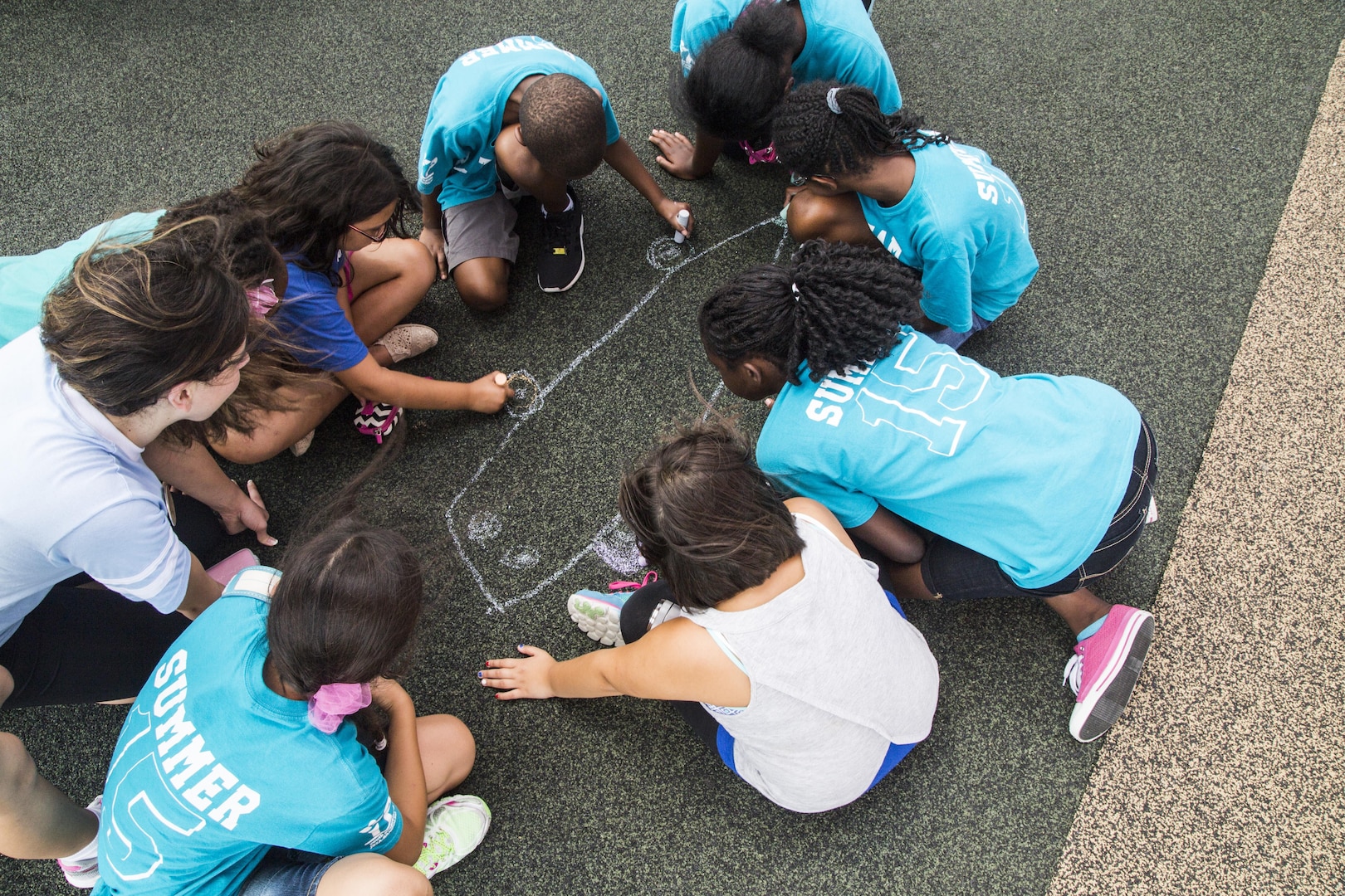 Liz Frost (left), Joint Base San Antonio-Randolph Youth Center assistant, helps a group of children start their own chalk drawing during an ‘Image Makers’ class July 8 at JBSA-Randolph. The class shows children how to both create a scene on the ground and have a partner capture them within the picture. (U.S. Air Force photo by Senior Airman Alexandria Slade/Released)