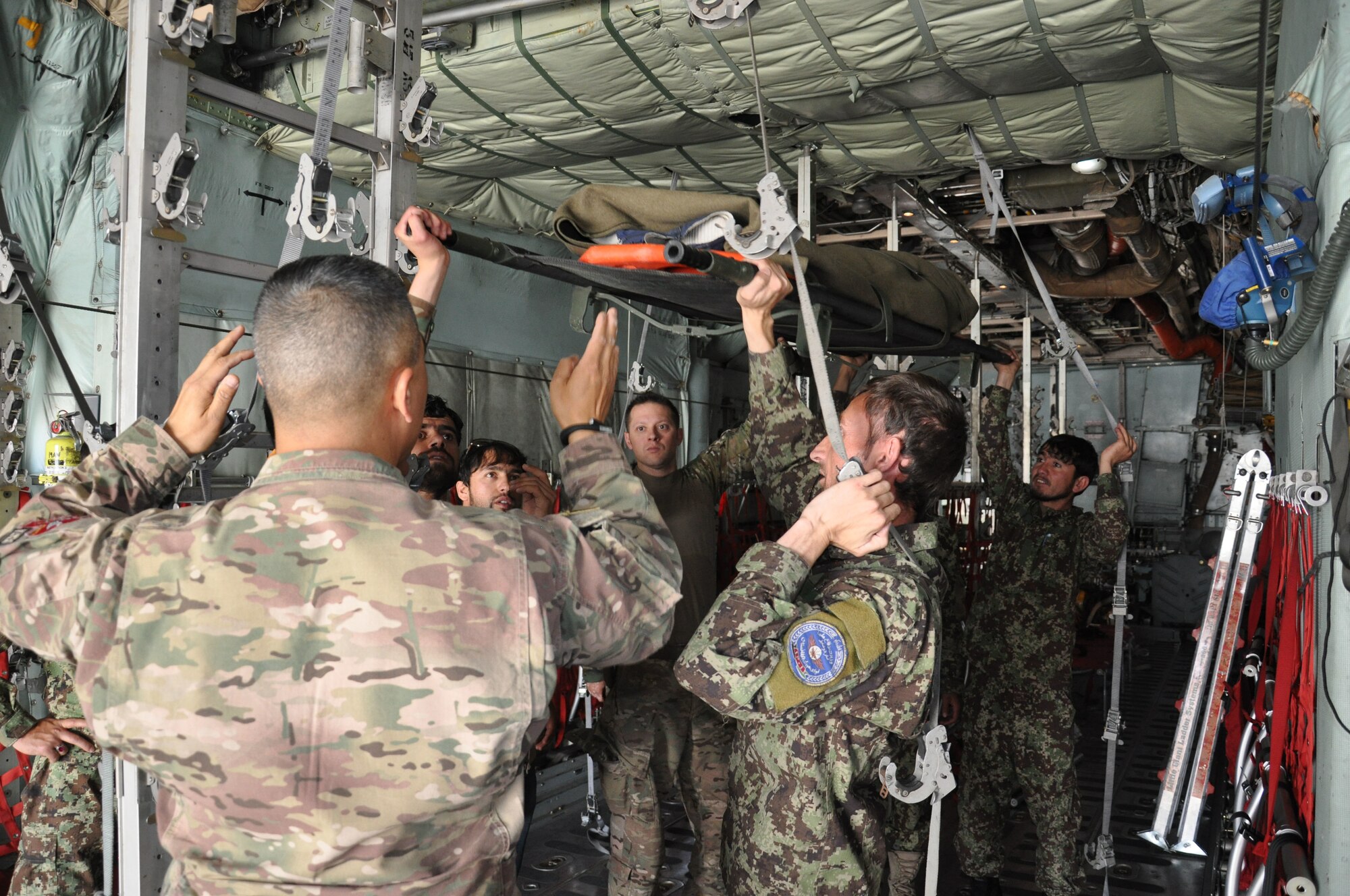 Train, Advise, Assist Command – Air (TAAC-Air) advisers provide instruction to the Afghan National Army flight medics while reconfiguring the cargo compartment of a C-130H Hercules from netted seating to metal stanchions that hold stretchers for a “simulated” medical evacuation, or medevac, flight at Hamid Karzai International Airport, July 9, 2015. TAAC-Air advisers provide weekly training to the ANA and Afghan air force to further develop and grow their fight medics capabilities. (U.S. Air Force photo/Capt. Eydie Sakura/released)