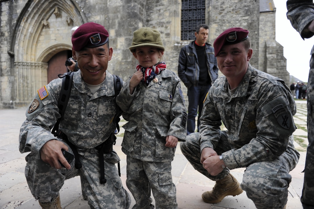 U.s. Army Sgt. First Class Andy Yoshimura and Sgt. First Class Dan Stroupe from USACAPOC(A), pose with a local girl in front of the church of Ste. Mere Eglise where Sgt. John Steele landed on D-Day on June 3, 2014. They are visiting Ste. Mere Eglise, France for the upcoming 70th anniversary of the D- day invasion. (U.S. Army Photo By Spc. Joshua E. Powell)