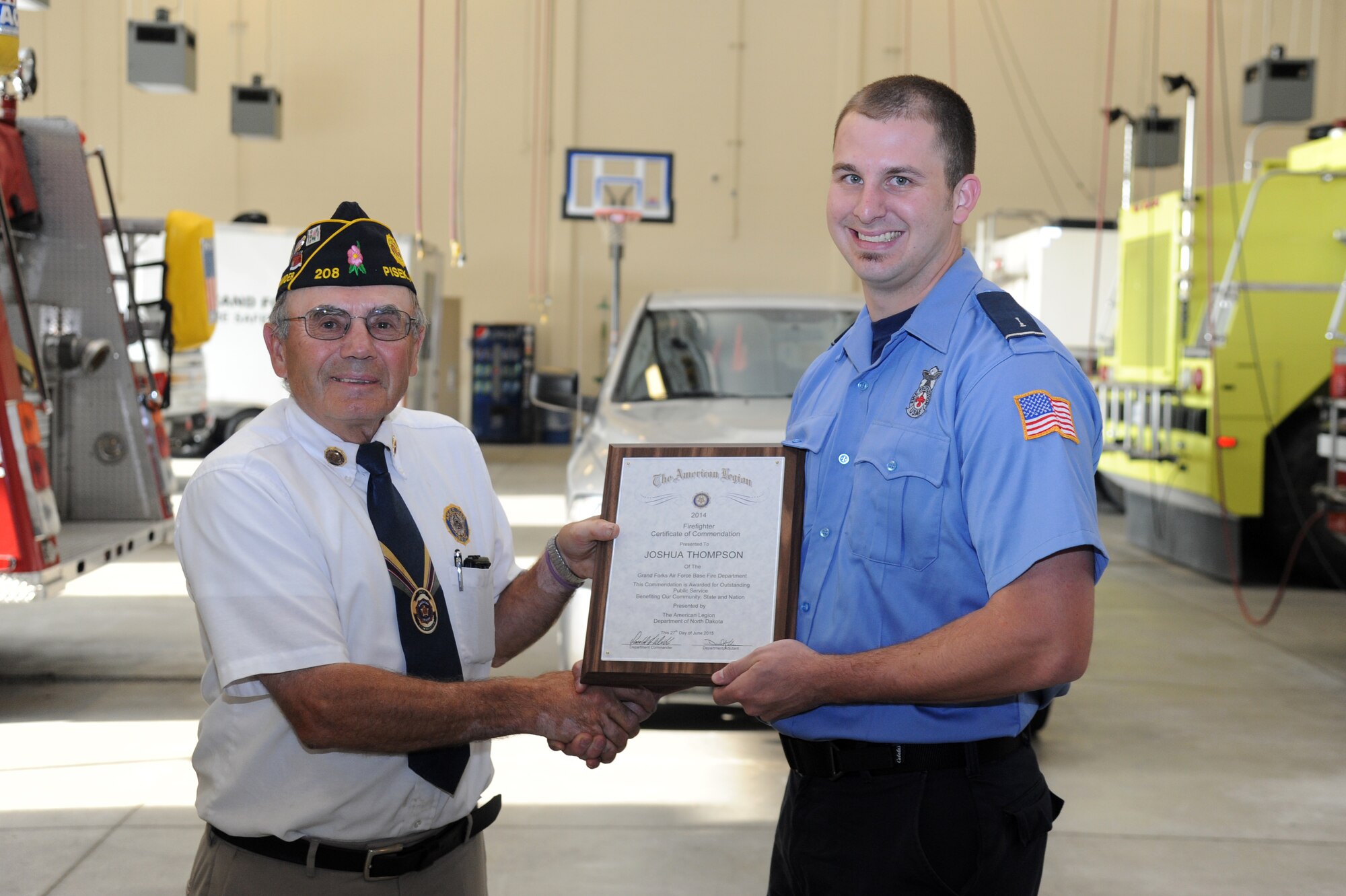 Joshua Thompson, 319th Civil Engineer Squadron firefighter, receives the 2014 American Legion Fire Fighter of the Year Award from Eugene Kachena, past American Legion Department of North Dakota commander, in the 319th CES Fire Department on Grand Forks Air Force Base, N.D., July 15, 2015. Kachena traveled from Pisek, N.D., to present the award to Thompson in the presence of his co-workers and unit leadership during morning roll call. This is the third consecutive year the American Legion has presented their Fire Fighter of the Year award to an individual from the Grand Forks AFB Fire Department. (U.S. Air Force photo by Tech. Sgt. David Dobrydney/released)