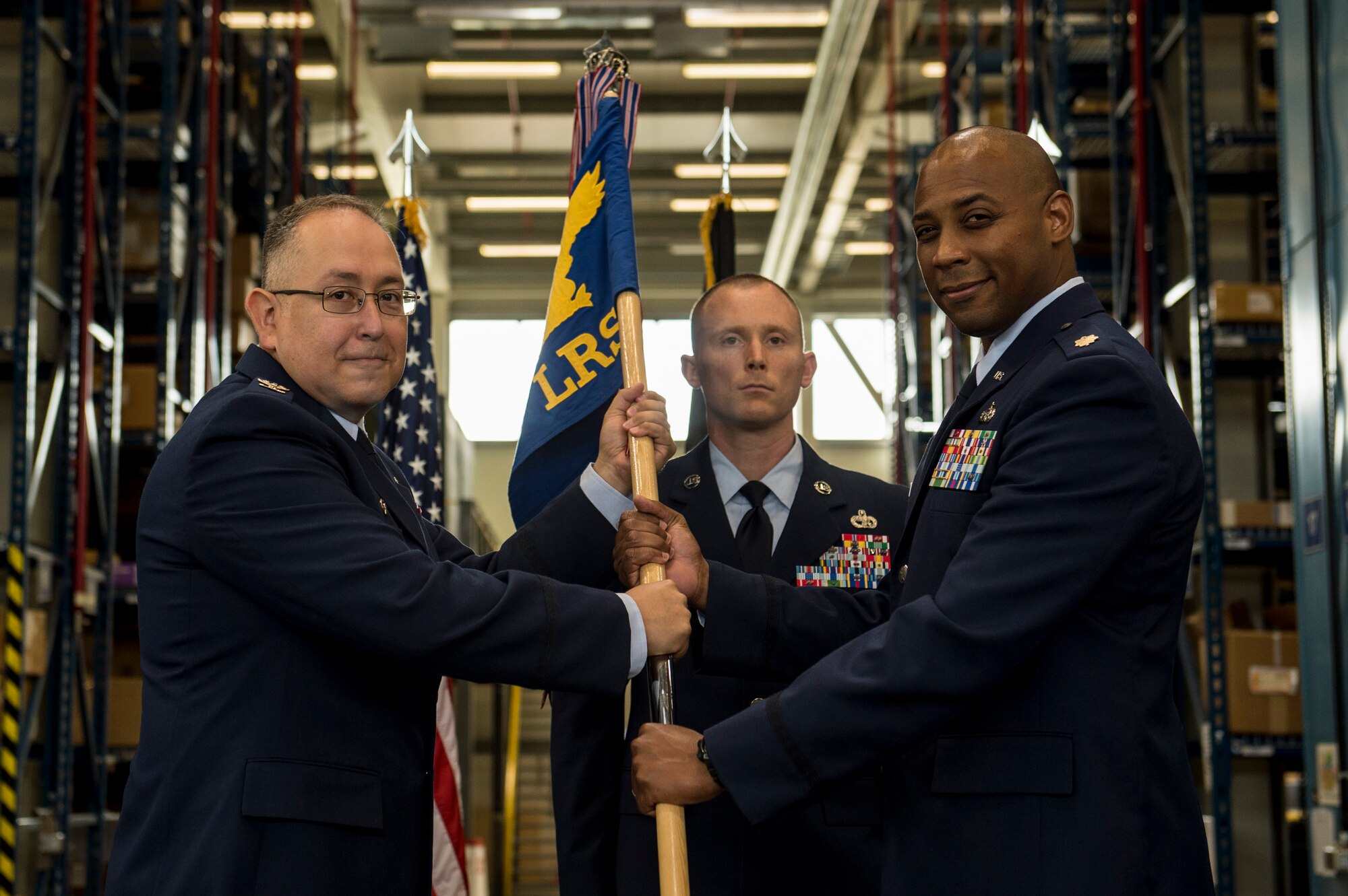U.S. Air Force Col. Drysdale Hernandez, 52nd Mission Support Group commander left, hands the ceremonial guidon to U.S. Air Force Maj. Andre Bradley, the incoming 52nd Logistics Readiness Squadron commander, during the 52nd LRS change of command ceremony inside an LRS warehouse on Spangdahlem Air Base, Germany, July 8, 2015. Bradley assumed command from former commander, U.S. Air Force Lt. Col. Phillip Noltemeyer. (U.S. Air Force photo by Senior Airman Rusty Frank/Released)