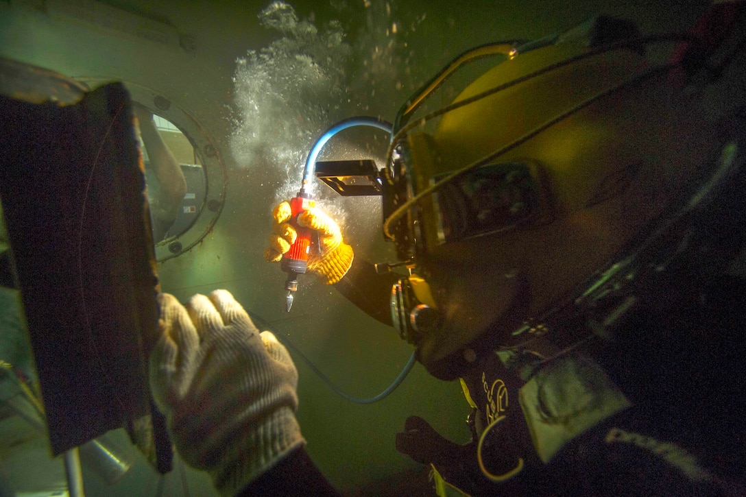 Navy Petty Officer 3rd Class Phil Wall uses a burr grinder to remove minor flaws during an underwater welding project in Miami, Florida, July 13, 2015. Wall is a construction electrician assigned to Underwater Construction Team 2.
