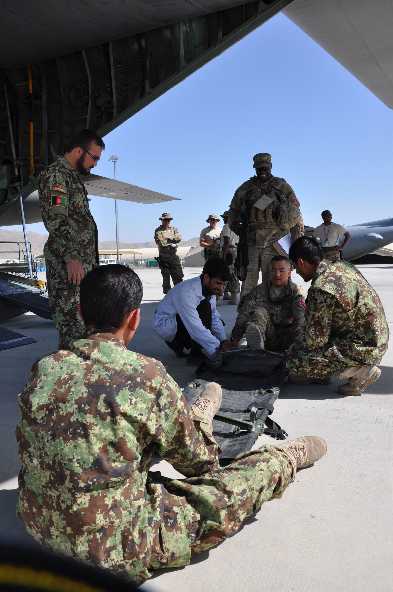 Col. (Dr.) Sarady Tan, Train, Advise, Assist Command – Air (TAAC-Air) command surgeon general (center ground), uses his feet to push open a medical litter, or stretcher, to use during training in the back of a C-130H Hercules at Hamid Karzai International Airport, July 9, 2015. Tan is deployed to Kabul from Mountain Home Air Force Base, Idaho. (U.S. Air Force photo/Capt. Eydie Sakura/released)