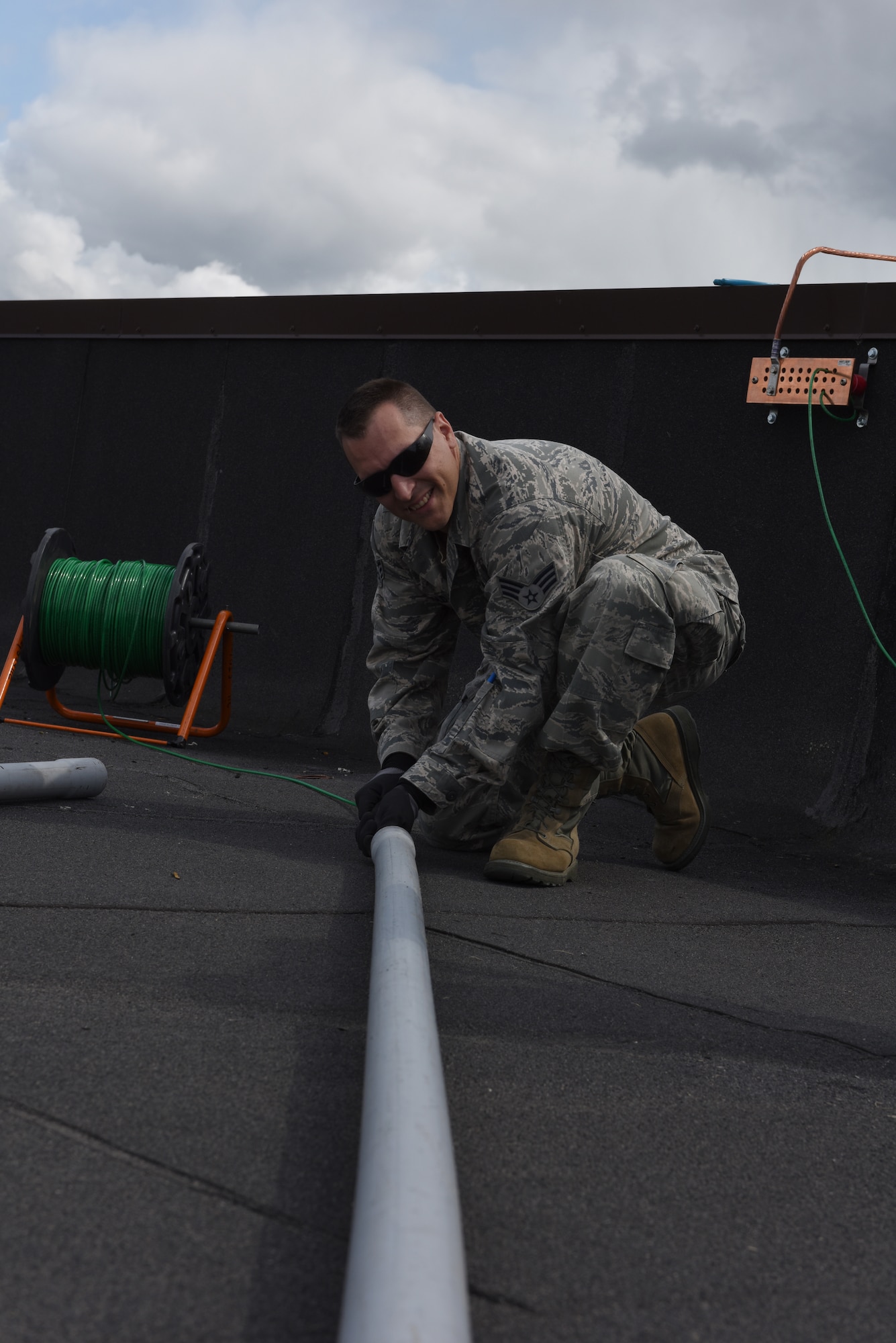 Senior Airman Mathew Gold, cable and antenna systems technician, 211th Engineering Installation Squadron, runs a cable line through PVC piping as part of the antenna work on the roof of Hanger 18 at Joint Base Elmendorf-Richardson, Anchorage, Alaska. Gold is one of the Airmen participating in Exercise Frosty Spear, where the 211th EIS is providing cyberspace systems integrator support to the 176th Wing, Joint Base Elmendorf-Richardson. (U.S. Air National Guard photo by Staff Sgt. Claire Behney/Released)