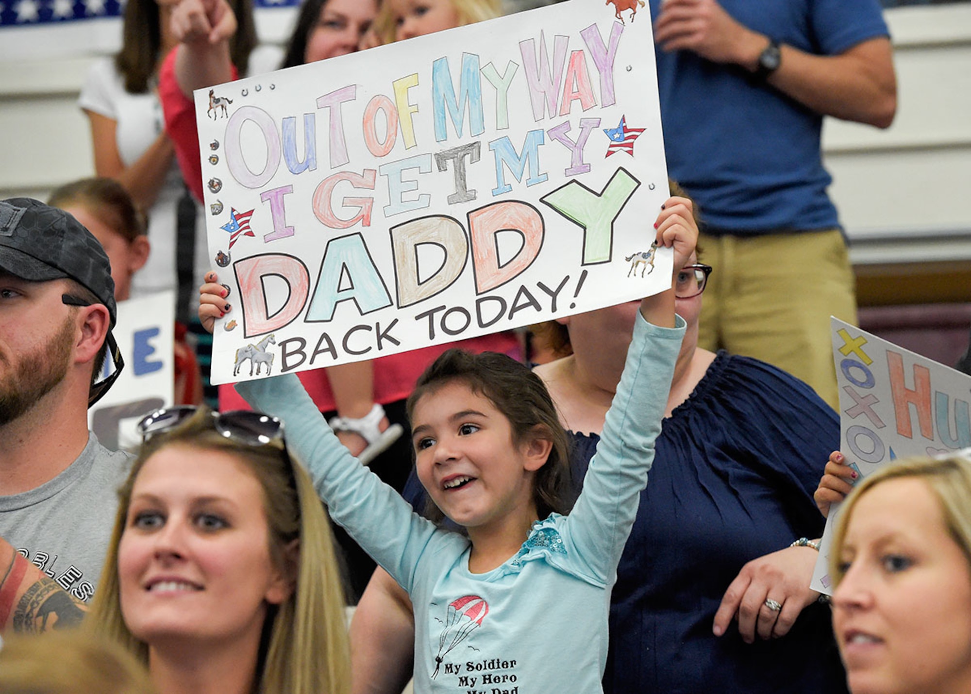 Danya Livermore, 5, from Glide, Ore., waves a sign as Soldiers assigned to Headquarters and Headquarters Company, 1st Squadron (Airborne), 40th Cavalry Regiment, arrive during a redeployment ceremony on Joint Base Elmendorf-Richardson, Alaska, July 10, 2015. Danya's father, Sgt. 1st Class Steve Livermore and fellow Soldiers returned from a 10 month deployment in support of peacekeeping operations in Kosovo. (U.S. Air Force photo/Alejandro Pena)