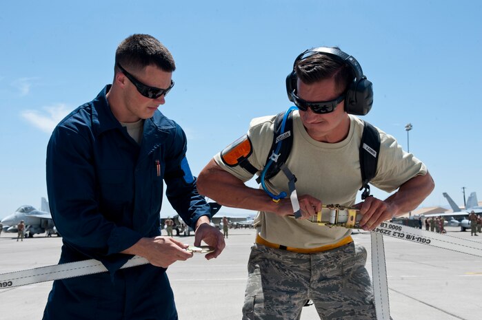 Senior Airman Justin Dufreche and Airman 1st Class Cameron Harris, both 159th Maintenance Squadron crew chiefs, Louisiana Air National Guard, pull two straps together to fasten down an F-15 Eagle during Red Flag 15-3 at Nellis Air Force Base, Nev., July 14, 2015. Red Flag provides a series of intense air-to-air scenarios for aircrew and ground personnel to increase their combat readiness and effectiveness for future real-world operations. (U.S. Air Force photo by Airman 1st Class Jake Carter)