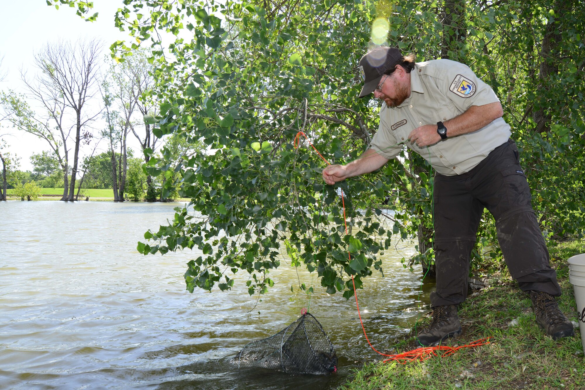 Chris Kennedy, U.S. Fish and Wildlife Service biologist, lifts a cage designed to capture fish, July 15, 2015, at McConnell Air Force Base, Kan. The biologists captured fish to make sure they are healthy, check if they are reproducing and to see if the pond needs to be restocked to improve the fishery. (U.S. Air Force photo by Airman 1st Class Christopher Thornbury)
