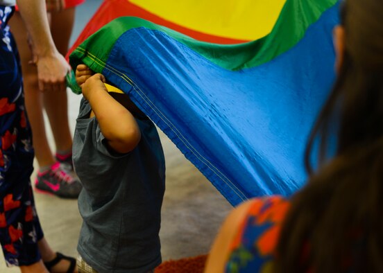 A child plays with a multicolored parachute during JAM Summer Camp, July 14, 2015, at Aviano Air Base, Italy. The class incorporated color-recognition and active exercises in addition to playing with musical instruments. (U.S. Air Force photo by Senior Airman Austin Harvill/Released)