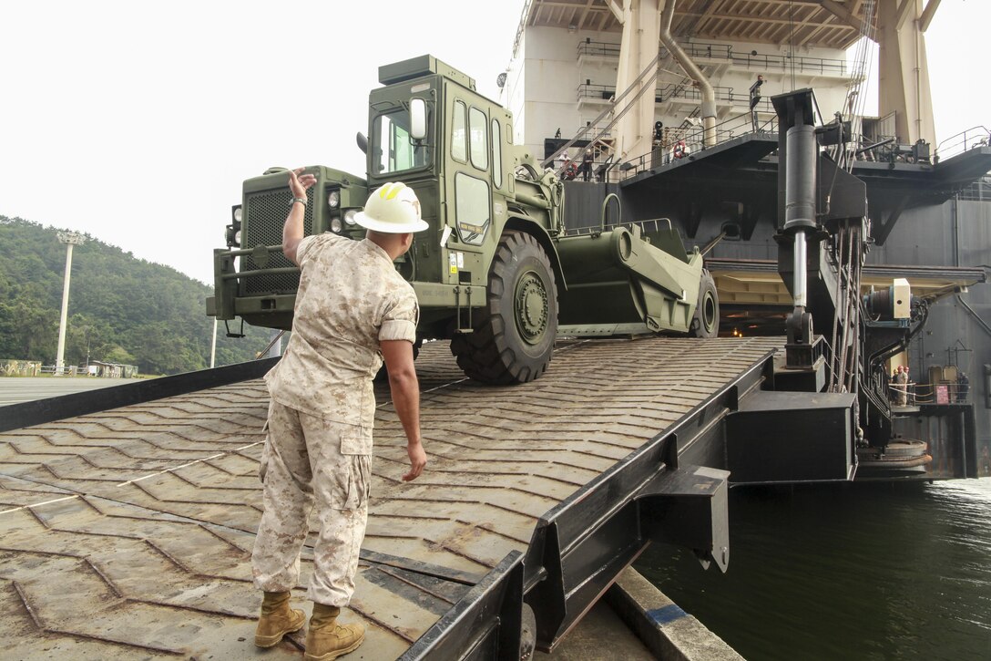U.S. Marine Corps Gunnery Sergeant Sergio D. Barrios, the Offload Preparation Party (OPP) SNCOIC aboard the USNS 2nd Lt. John P. Bobo, III Marine Expeditionary Force, ground guides a 120-M grader during the MPF Offload of gear and equipment from the Bobo in Chinhae, South Korea, June 13, 2015 in support of Peninsula Express 15. Peninsula Express is one in a series of regularly-scheduled combined, small-unit, tactical training exercises that demonstrates continued dedication to the ROK-U.S. relationship, contributing to the security and stability of the Korean Peninsula and Asia-Pacific region. (U.S. Marine Corps photo by Sgt. Justin A. Bopp/Released)