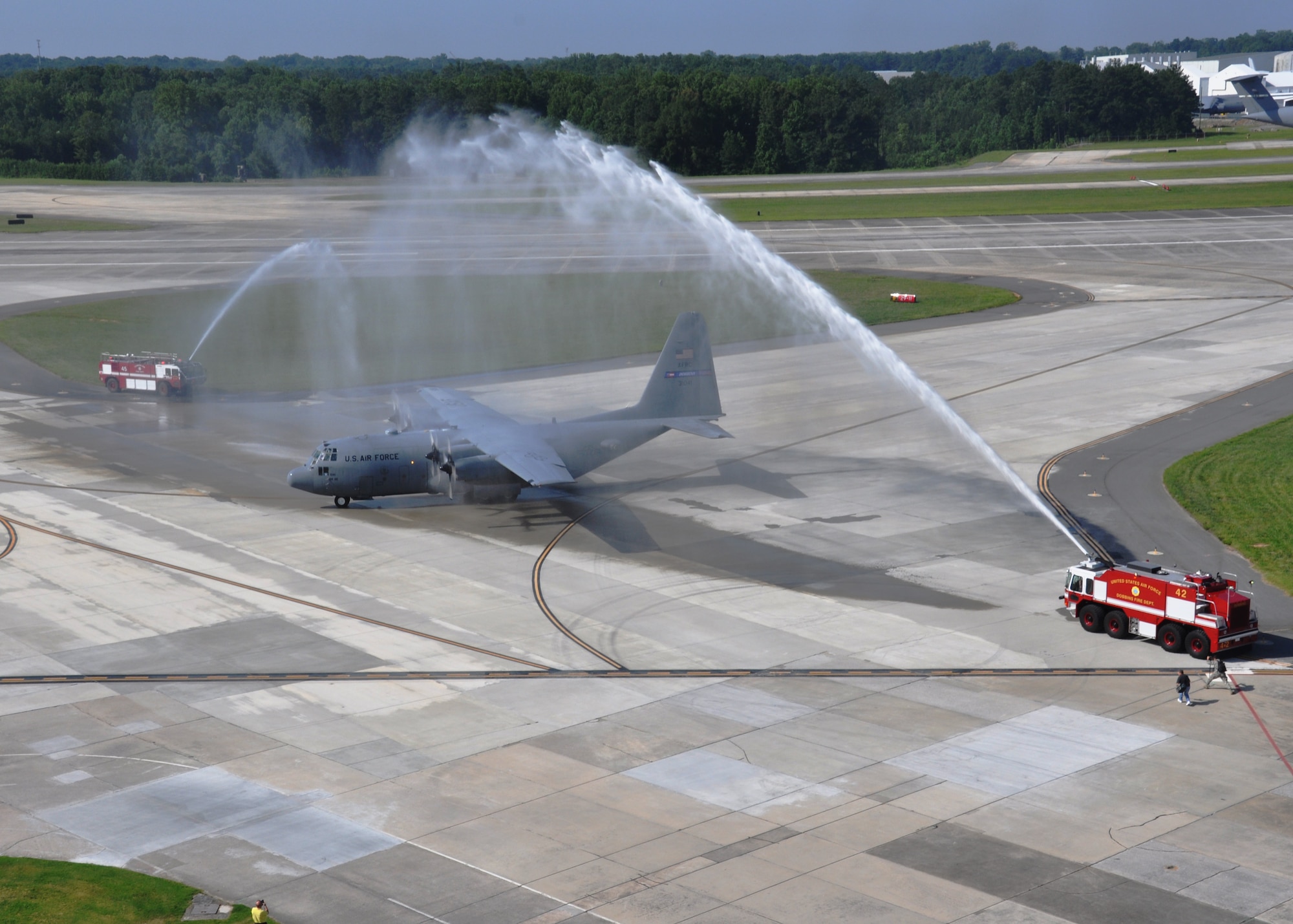 Fire trucks spray an arc of water over a C-130 Hercules after it lands at Dobbins Air Reserve Base, Ga., July 11, 2015. Col. Brett Clark, 94th Airlift Wing commander, flew the plane for his last flight before he retired and was greeted with a salute of water from the base fire department. (US Air Force Photo/ Senior Airman Miles Wilson)