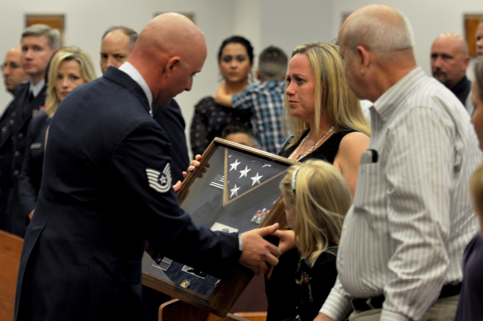 The 17th Security Forces Squadron presents Michele Kelley with a shadowbox at the Memorial Service in Honor of her husband, Tech. Sgt. Christopher Kelley, at the Taylor Chapel on Goodfellow Air Force Base, Texas, July 16, 2015. Kelley, an individual mobilization augmentee for the 17 SFS, was killed in the line of duty as a Hutto, Texas police officer. (U.S. Air Force photo by Senior Airman Joshua Edwards/Released)