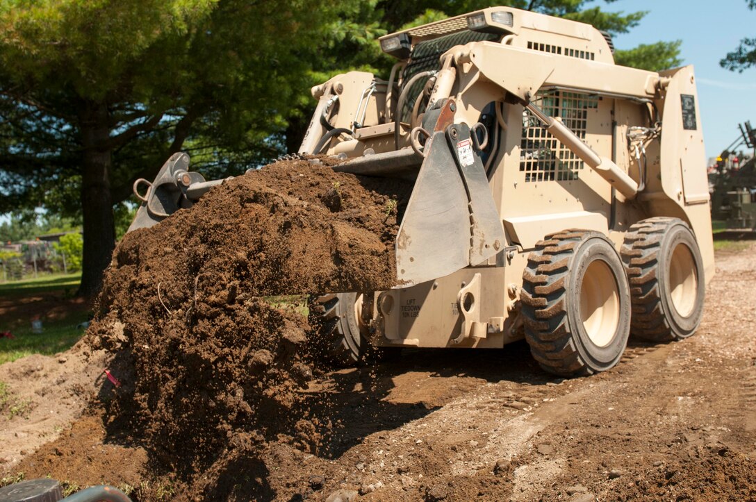 A soldier uses a skid-steer loader to bury a polyvinyl chloride, or PVC, pipe while preparing a parking lot on Camp Johnson in Colchester, Vt., July 16, 2015. The soldier is assigned to the Massachusetts Army National Guard's 189th Engineer Team Asphalt, which is paving parking lots at National Guard armories throughout Vermont as part of its annual training.