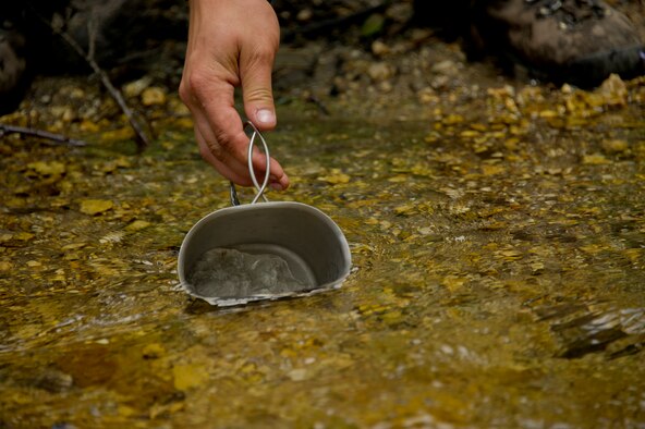 Airman 1st Class Zachary Mikolajczyk, 22nd Training Squadron Survival, Evasion, Resistance and Escape specialist, demonstrates how to properly collect water from a stream with a canteen cup, June 13, 2015, in the Colville National Forest, Wash. Students learned that water procurement is an important asset to survival: the human body can only sustain life for three days without any water. (U.S. Air Force photo/Airman 1st Class Nicolo J. Daniello)