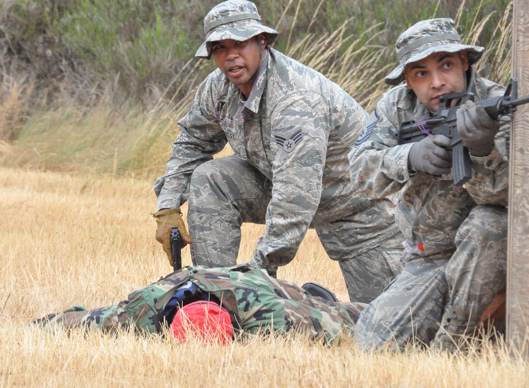 From left, Senior Airman Paul Whatley, 446th Aeromedical Staging Squadron medical technician, secures a mannequin patient while Master Sgt. James Millan, also 446th ASTS medical technician, provides protection from mock enemy fire July 13 at the South 40, South Approach, here. Airmen from the 446th ASTS completed tactical combat casualty care training as part of their annual training requirements in an exercise dubbed “Care Under Fire.”