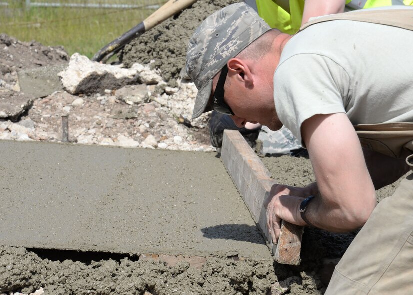 U.S. Air Force Senior Airman Stephen Beasley, 100th Civil Engineer Squadron Pavements and Equipment journeyman from Wakeforest, N.C., removes any excess concrete from a path being laid June 18, 2015, on RAF Mildenhall, England. The wooden screed board was used by two Airmen working together sliding the board back and forth along the two preplaced forms that are used to hold the concrete in place while it dries. (U.S. Air Force photo by Gina Randall/Released)