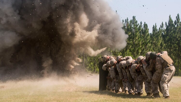 Marines with 2nd Combat Engineer Battalion and 1st Battalion, 8th Marine Regiment crouch behind a protective blanket after detonating a breaching charge during the urban breaching portion of a demolition package at Marine Corps Base Camp Lejeune, North Carolina, July 10, 2015. The demolition package was conducted in preparation for an upcoming deployment, where the two units will be working together in support of Special-Purpose Marine Air-Ground Task Force Crisis Response- Africa. 
