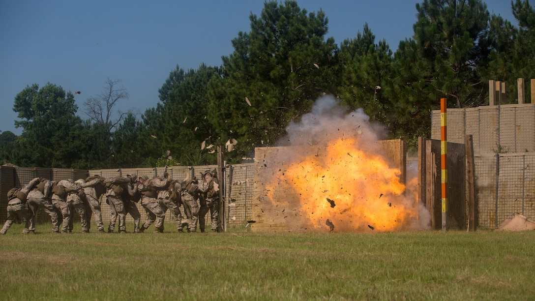 Marines with 2nd Combat Engineer Battalion and 1st Battalion, 8th Marine Regiment crouch behind a protective blanket shielding them from the explosion during the urban breaching portion of a demolition package at Marine Corps Base Camp Lejeune, North Carolina, July 10, 2015. The demolition package was conducted in preparation for an upcoming deployment, where the two units will be working together in support of Special-Purpose Marine Air-Ground Task Force Crisis Response- Africa. 