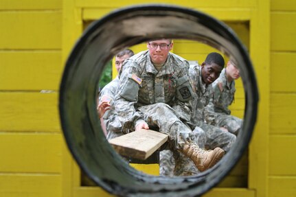 Cadets of the 7th Regiment work together to build a bridge using boards, to cross one by one through the tunnel of an obstacle July 14, at the Dunegan Team Development Course, Fort Knox, Ky. The course tests the cadets on their ability to solve complex, tactically relevant problems using teamwork and communication.