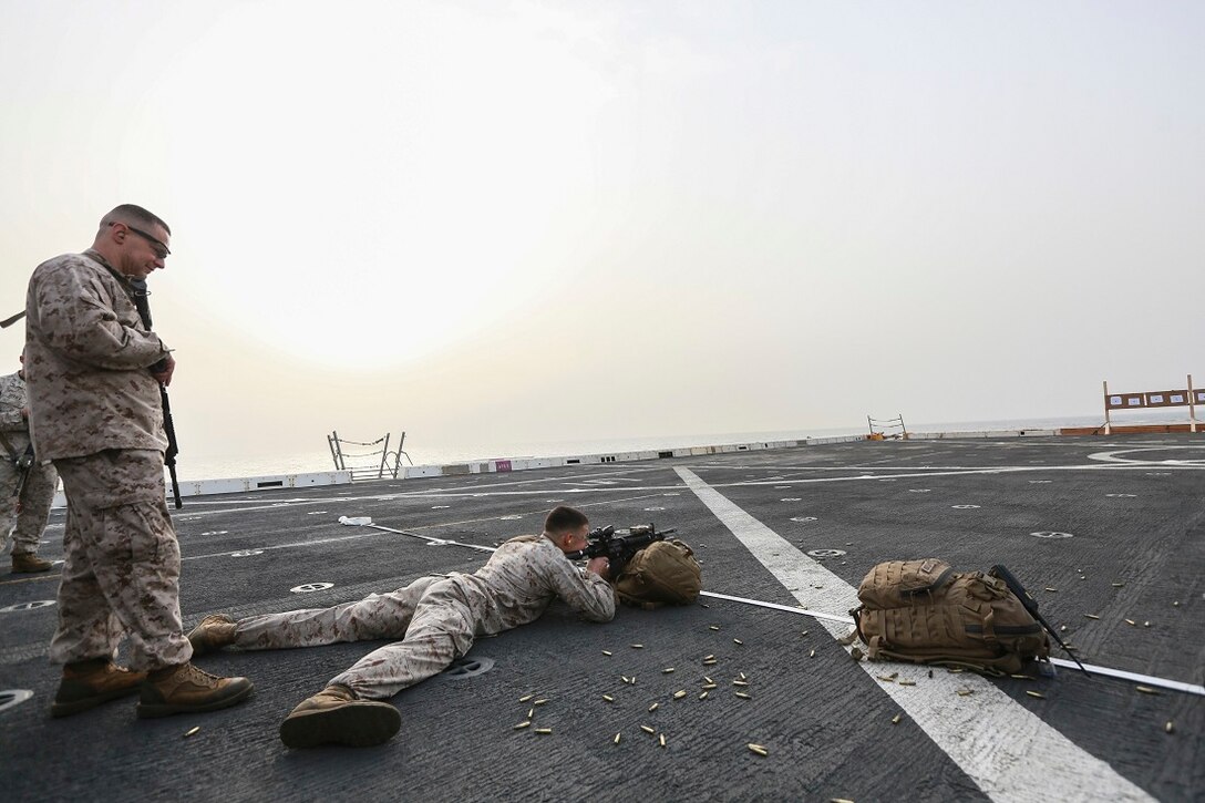 U.S. Marine Gunnery Sgt. Dragos Coca, left,  observes as Cpl. Michael Odintz fires his weapon to find his battle-sight zero on the flight deck of the amphibious transport dock ship USS Anchorage (LPD 23). Coca is a platoon sergeant and Odintz is a squad leader, both with Light Armored Reconnaissance Detachment, Battalion Landing Team 3rd Battalion, 1st Marine Regiment, 15th Marine Expeditionary Unit. The Marines with LAR Detachment are part of the ground combat element of the 15th MEU, and embarked aboard the ships of the Essex Amphibious Ready Group, are deployed in support of maritime security operations and theater security cooperation efforts in the U.S. 5th Fleet area of operations. (U.S. Marine Corps photo by Sgt. Steve H. Lopez/ Released)