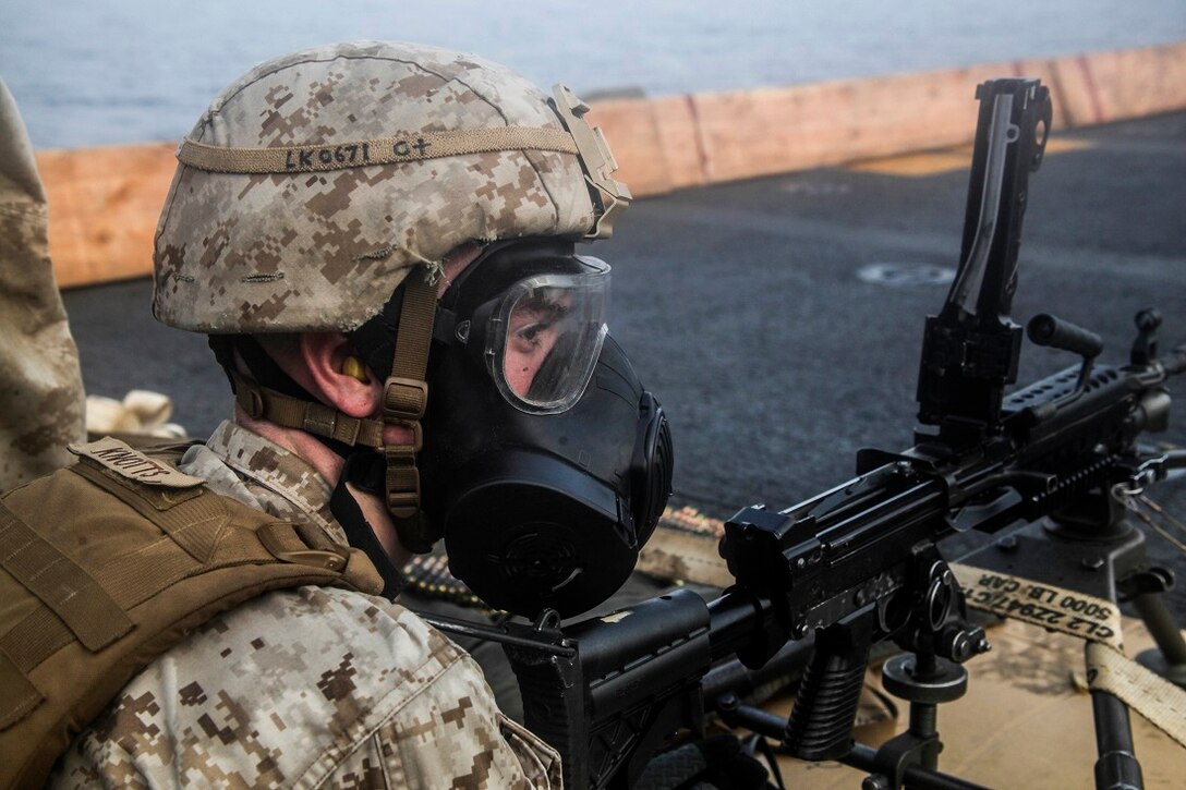 GULF OF ADEN (July 14, 2015) U.S. Marine Lance Cpl. Tyler Knotts dons his gas mask before firing an M240B machine gun at targets on the flight deck of the amphibious assault ship USS Essex (LHD 2). Knotts is a machine gunner with Lima Company, Battalion Landing Team 3rd Battalion, 1st Marine Regiment, 15th Marine Expeditionary Unit. The 15th MEU is embarked on the Essex Amphibious Ready Group and is deployed to maintain regional security in the U.S. 5th Fleet area of operations.  (U.S. Marine Corps photo by Cpl. Elize McKelvey/Released)