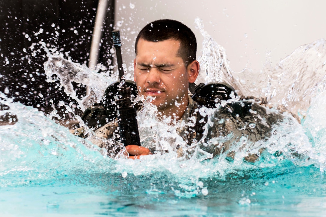 A soldier jumps in the swimming pool with a ruck sack and a dummy weapon during combat water survival training at Fort Hunter Liggett, Calif., July 17, 2015. 