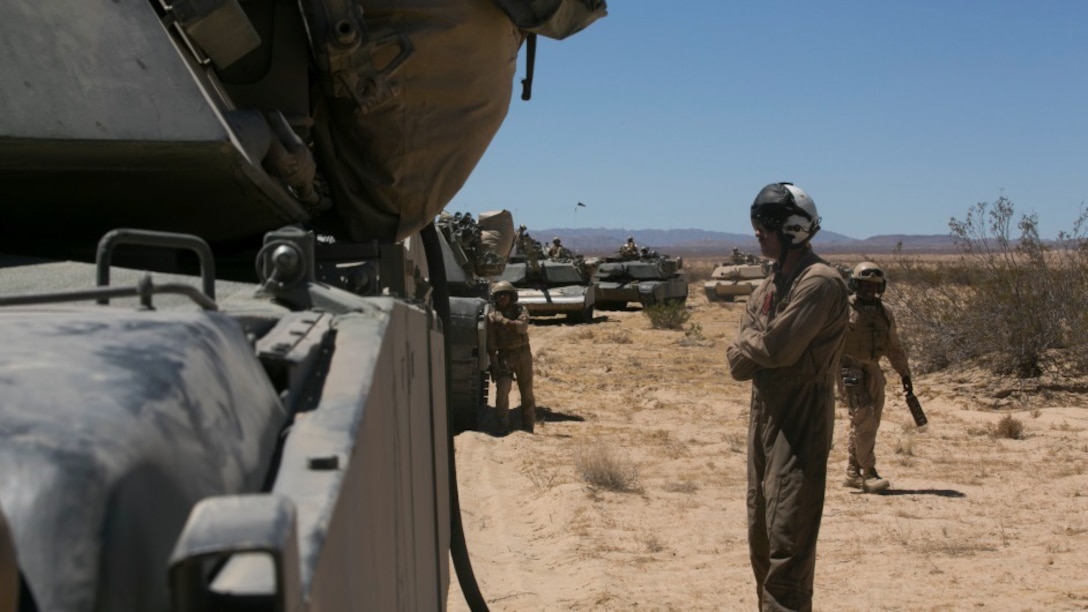 Sgt. Brandon Crist, crew chief, Marine Heavy Helicopter Squadron 465 waits by an M1A1 Abrams Tanks during a refueling exercise at Acorn Training Area, July 16, 2015. 1st Tanks conducted the exercise during their company’s gunnery examination. 