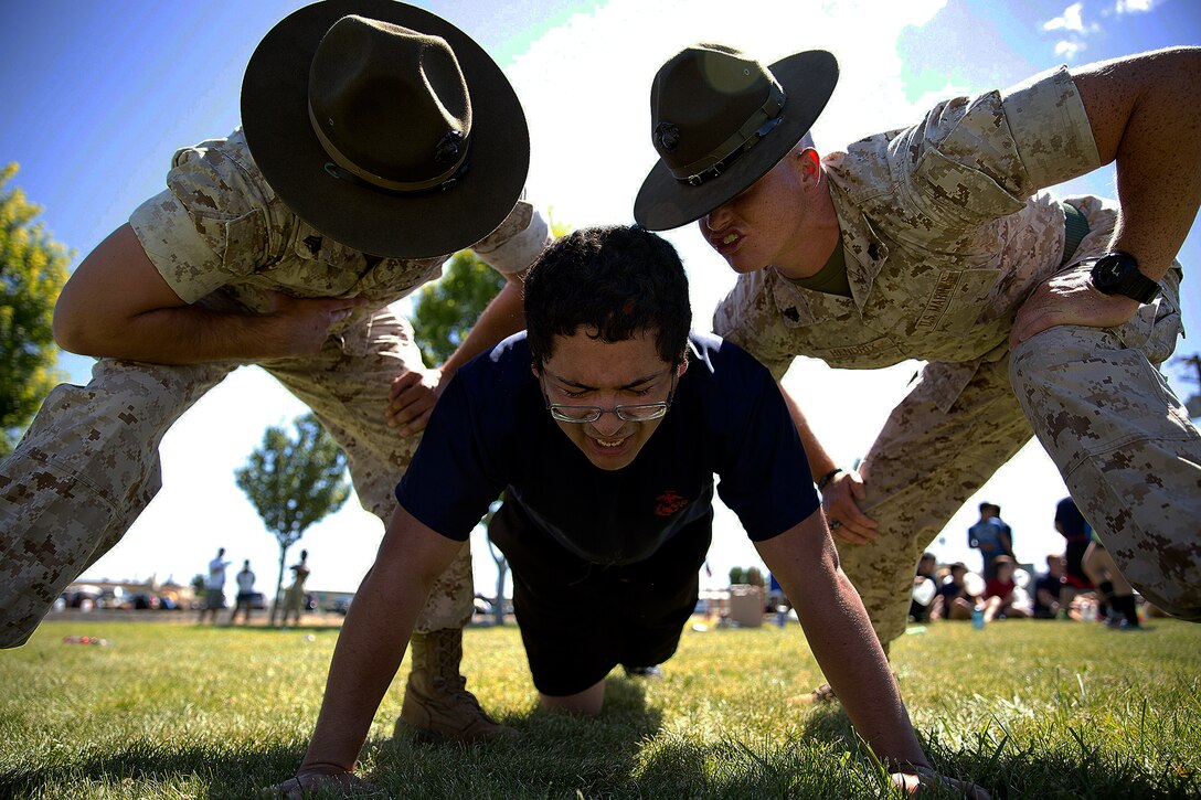 Marine Corps drill instructors Sgts. Stephen Wills, left, and Brandon Hendrix, motivate Jose Garcia, a Marine Corps enlistee from Yakima, Wash., during a Recruiting Station Seattle event at the Yakima Training Center in Yakima, July 17, 2015. Wills and Hendrix are assigned to Marine Corps Recruit Depot San Diego. 