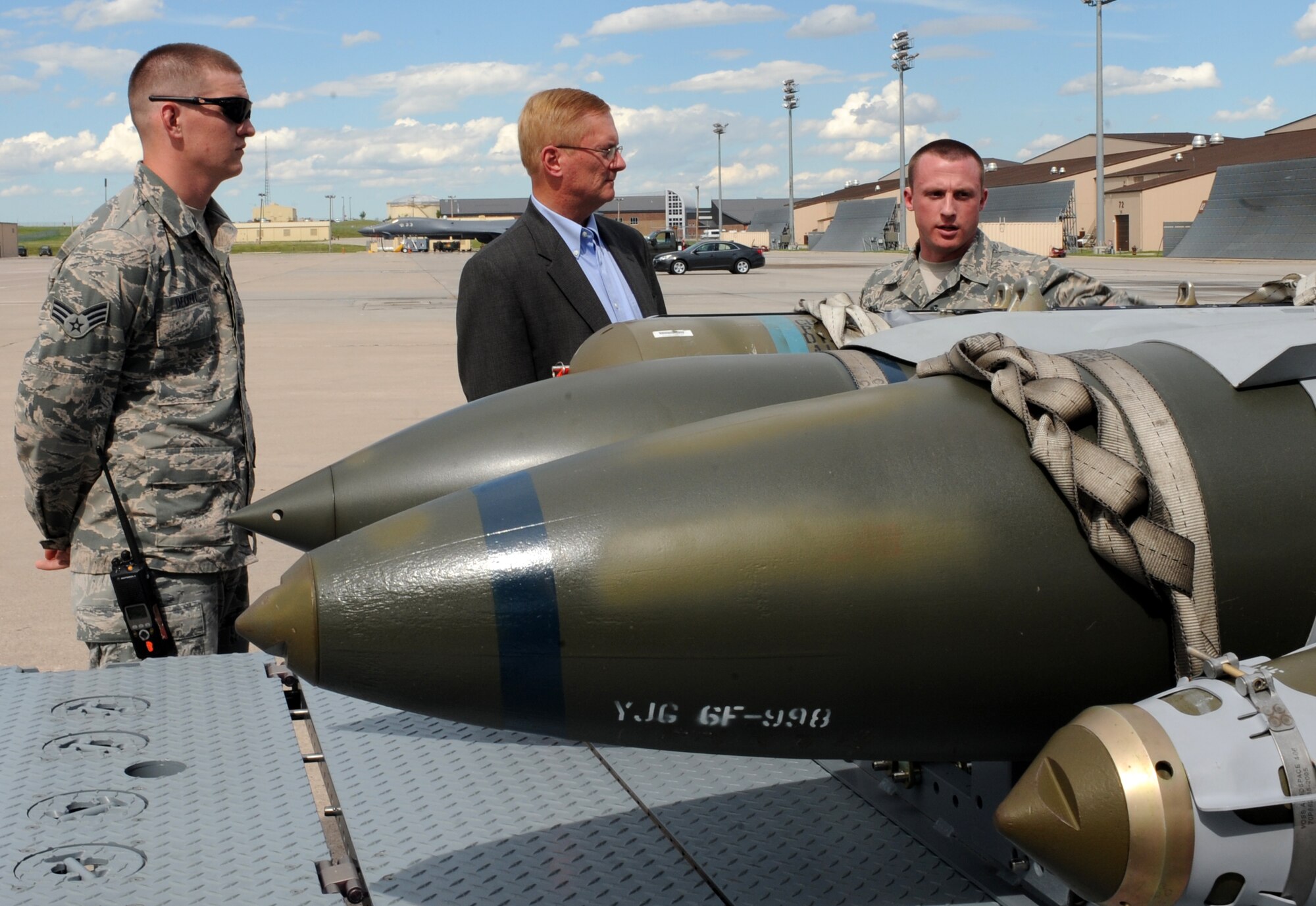 Senior Airman Andrew Deckert and Staff Sgt. Kyle Haun, 28th Munitions Squadron conventional maintenance crew chiefs, explain the characteristics of a cluster bomb unit and a laser Joint Direct Attack Munitions to Frank Beatty, spouse of Secretary of the Air Force Deborah Lee James, as part of a B-1 bomber static display at Ellsworth Air Force Base, S.D., July 20, 2015. During his visit to Ellsworth, Beatty visited the Youth Center, Higher Grounds, and B-One Yard thrift store in an effort to learn more about the quality of life initiatives for both Airmen and their families. (U.S. Air Force photo by Airman Sadie Colbert/Released)