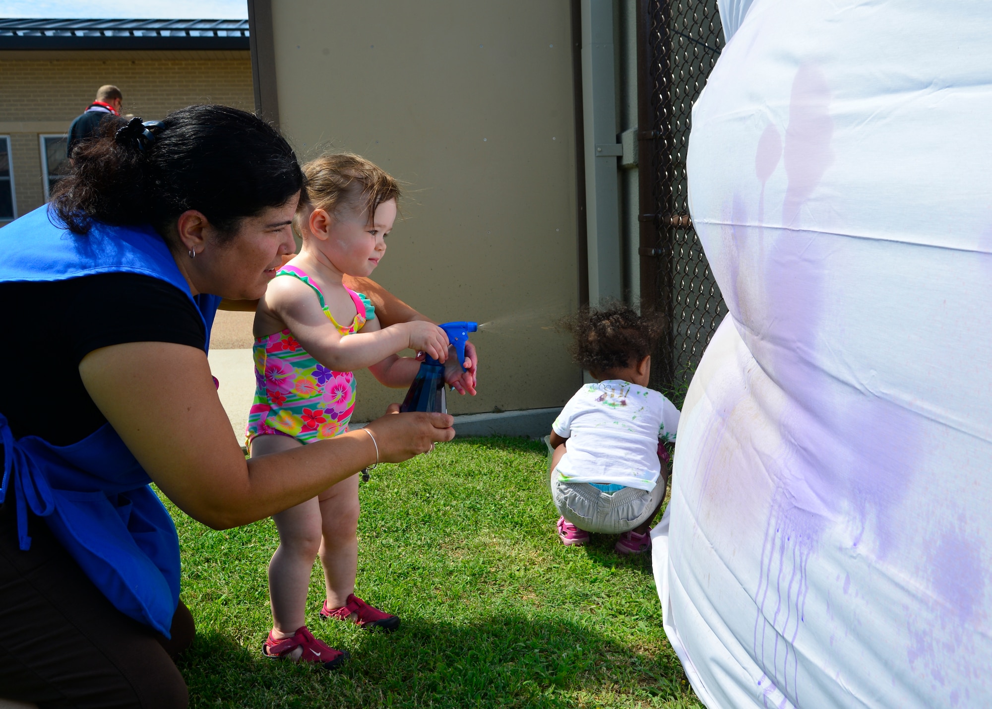 Rosa Sein-Lopez, Child Development Center caregiver, helps Livia Ellison spray a color dye onto a white sheet during the Pre Toddler Fun Day July 17, 2015, at the CDC on Dover Air Force Base, Del. Center staff and parents helped pre toddlers spray designs onto a sheet with an assortment of different colored dyes. (U.S. Air Force photo/Airman 1st Class William Johnson)