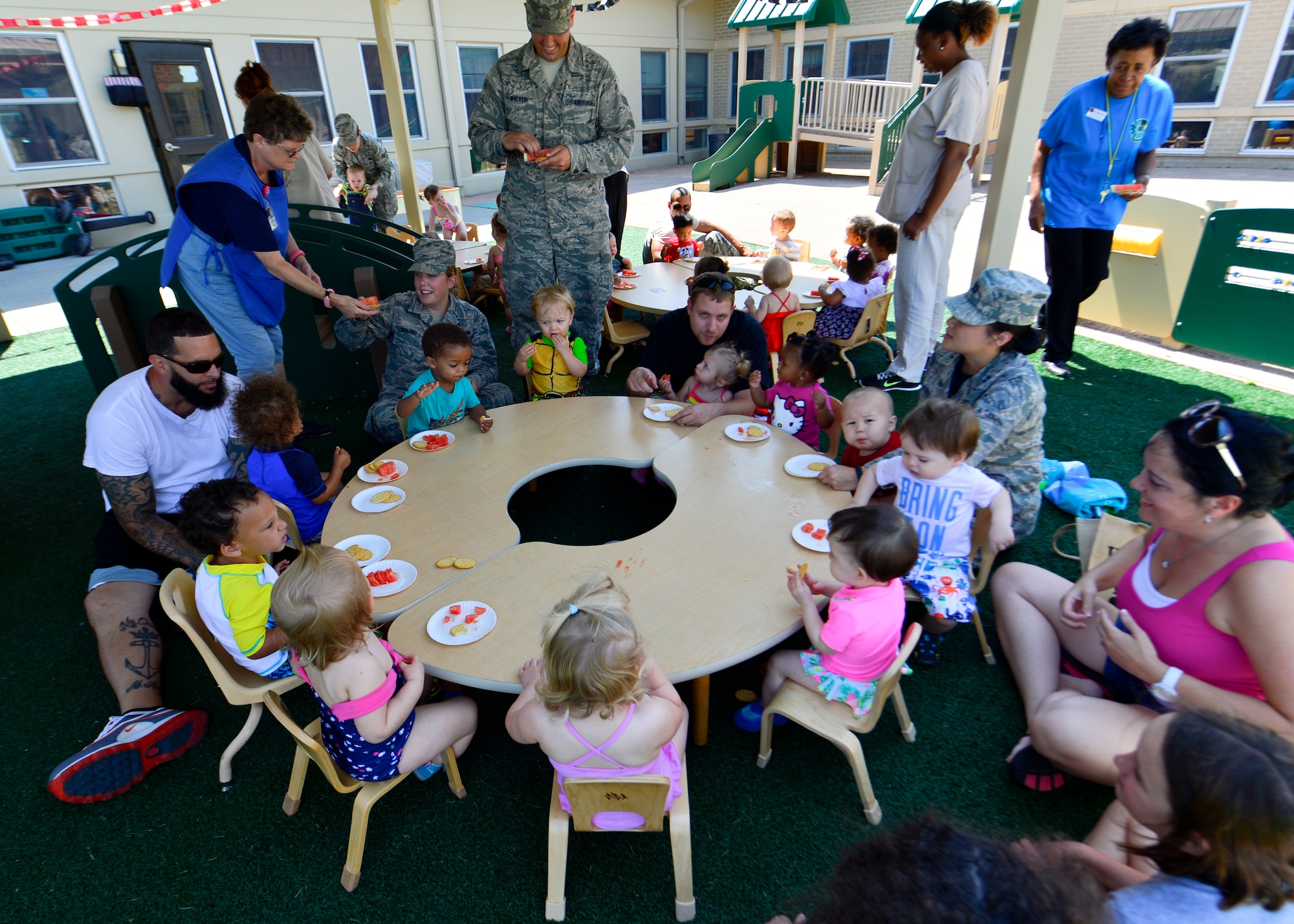 Parents and their children sit around a table to eat watermelon and crackers during the Pre Toddler Fun Day July 17, 2015, at the Child Development Center on Dover Air Force Base, Del. Parents were invited to spend time with their kids and participate in various outdoor activities during the day. (U.S. Air Force photo/Airman 1st Class William Johnson)