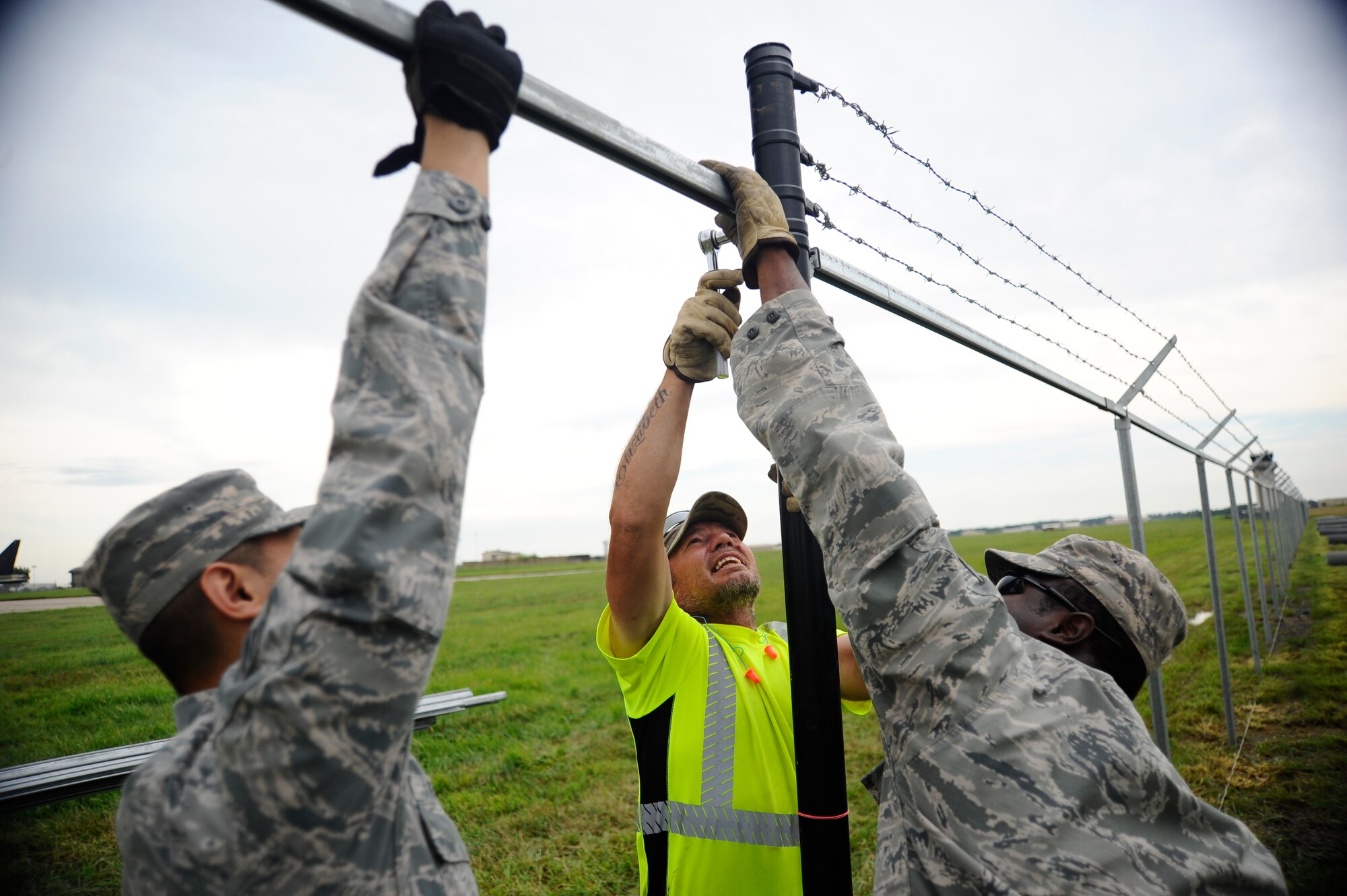 Senior Airman Michael Macaraig, left, and Senior Airman Willie Hatcher secure a top rail while Bobby Wren tightens it into place, July 22, 2015, at McConnell Air Force Base, Kan. Wren and the two Airmen, all 22nd Civil Engineer Squadron horizontal pavements shop heavy equipment operators, also known as “Dirt Boyz,” were constructing a new perimeter fence for the base. (U.S. Air Force photo by Senior Airman Victor J. Caputo)
