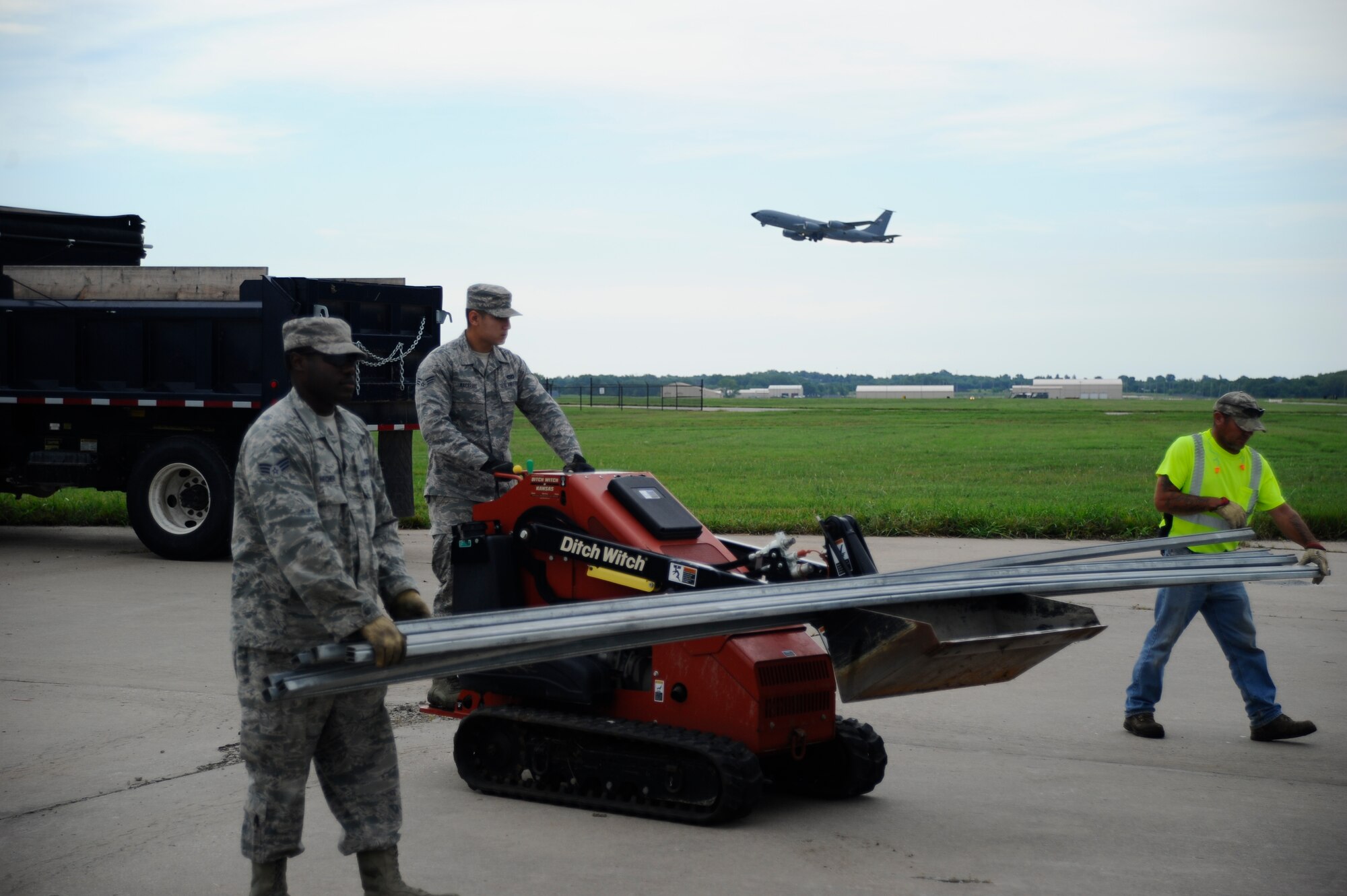 Senior Airman Willie Hatcher, left, Senior Airman Michael Macaraig, and Bobby Wren, 22nd Civil Engineer Squadron horizontal pavements shop heavy equipment operators, move a load of top rails for a fence while a KC-135 Stratotanker takes off behind them, July 22, 2015, at McConnell Air Force Base, Kan. The rails were used to connect posts on a new perimeter fence. (U.S. Air Force photo by Senior Airman Victor J. Caputo)