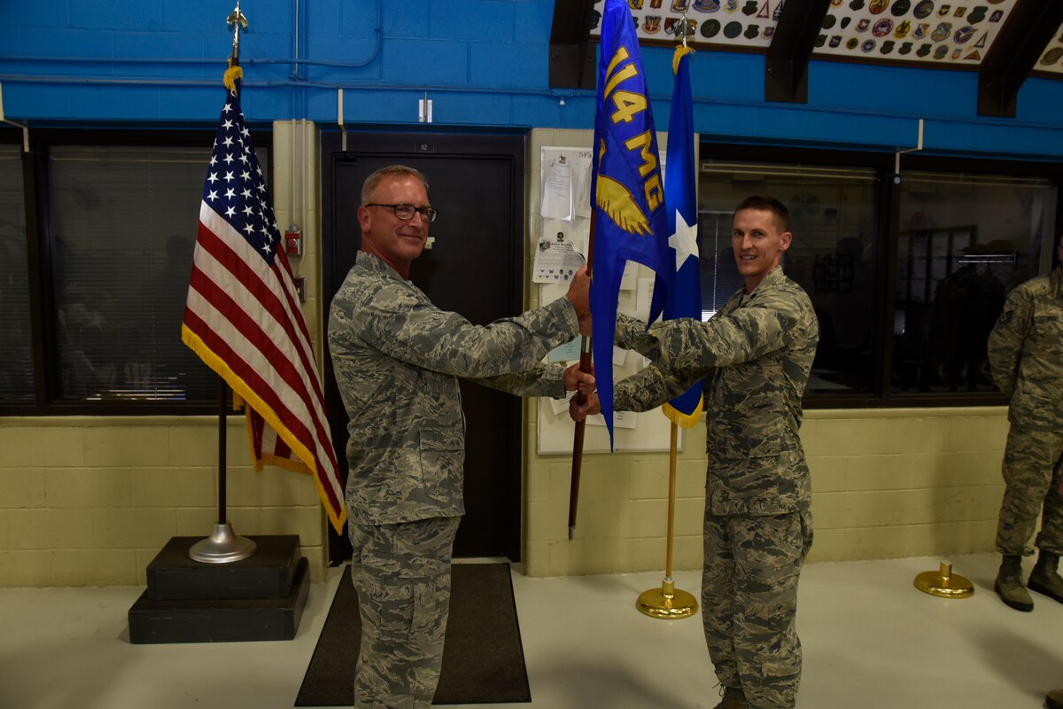 Col. Joel Degroot, 114th Maintenance Group commander, passes the 114th Maintenance Squadron (MXS) guidon to Lt. Col. Travis Boltjes, the incoming 114th MXS commander, during a change of command ceremony at Joe Foss Field, S.D., July 12, 2015. The primary purpose of a change of command ceremony is to allow subordinates to witness the formality of command change from one officer to another. The 114th MXS is the largest squadron on base with almost 250 Airmen. (National Guard photo by Staff. Sgt. Luke Olson/Released)