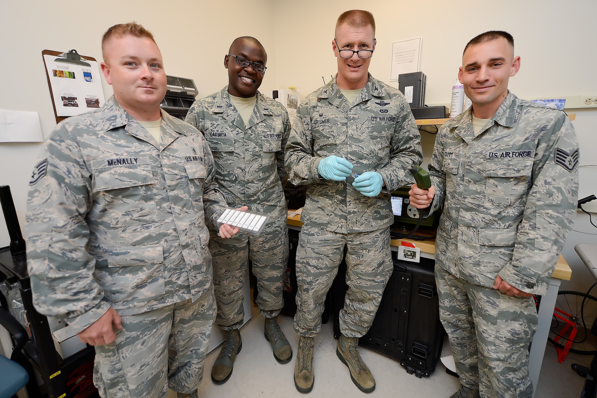 Col. Michael Grismer, 436th Airlift Wing commander, center, poses with members of the 436th Aerospace Medicine Squadron Biological Environmental Flight, during a visit to learn about their mission and capabilities July 17, 2015, at Dover Air Force Base, Del. Grismer wears medical gloves while handling a syringe during a test. From left to right are: Staff Sgt. Thomas McNally, Occupational Health Program NCO in charge, 1st Lt. Martin Gakuria, Bioenvironmental Engineering Flight deputy officer in charge and Staff Sgt. Jeffry Stamm, Readiness Flight NCO in charge. (U.S. Air Force photo/Greg L. Davis) 